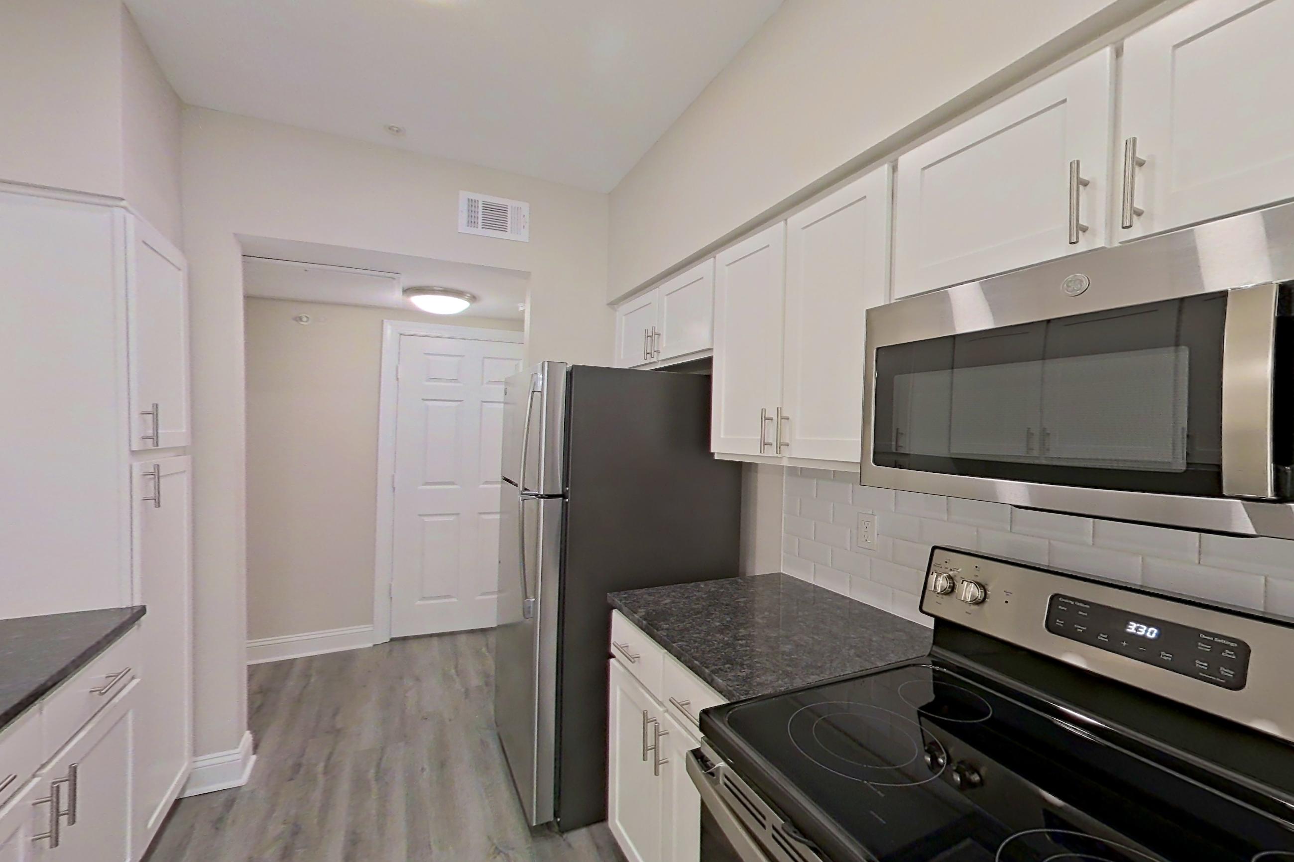 Kitchen with dark stone countertops, dishwasher, electric range, light countertops, light wood-finish flooring, microwave, oven/range, refrigerator, and stainless steel appliances, Apartment 5401 at Marq Perimeter