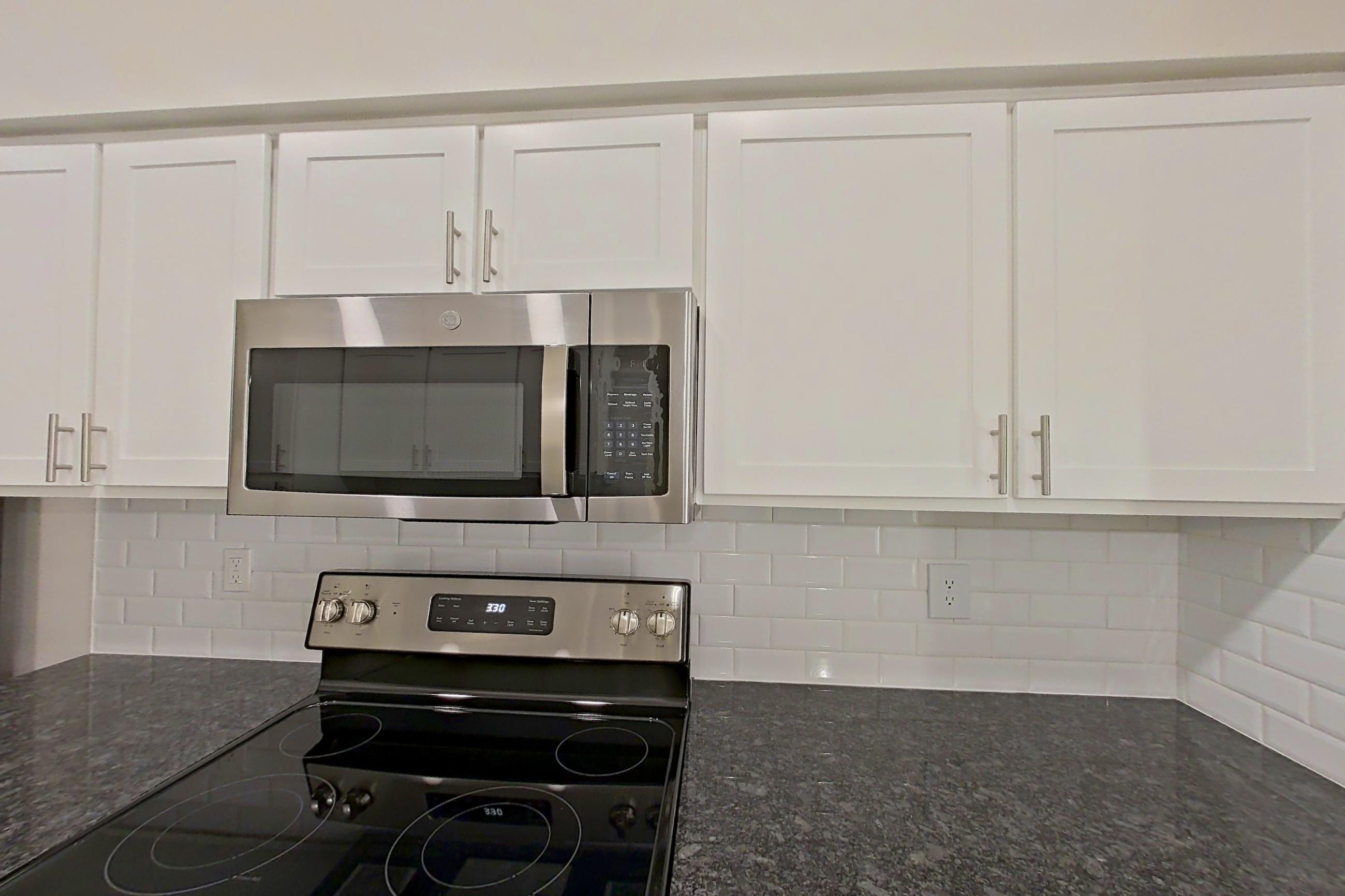 Kitchen with dark stone countertops, dishwasher, electric range, light countertops, light wood-finish flooring, microwave, oven/range, refrigerator, and stainless steel appliances, Apartment 5401 at Marq Perimeter