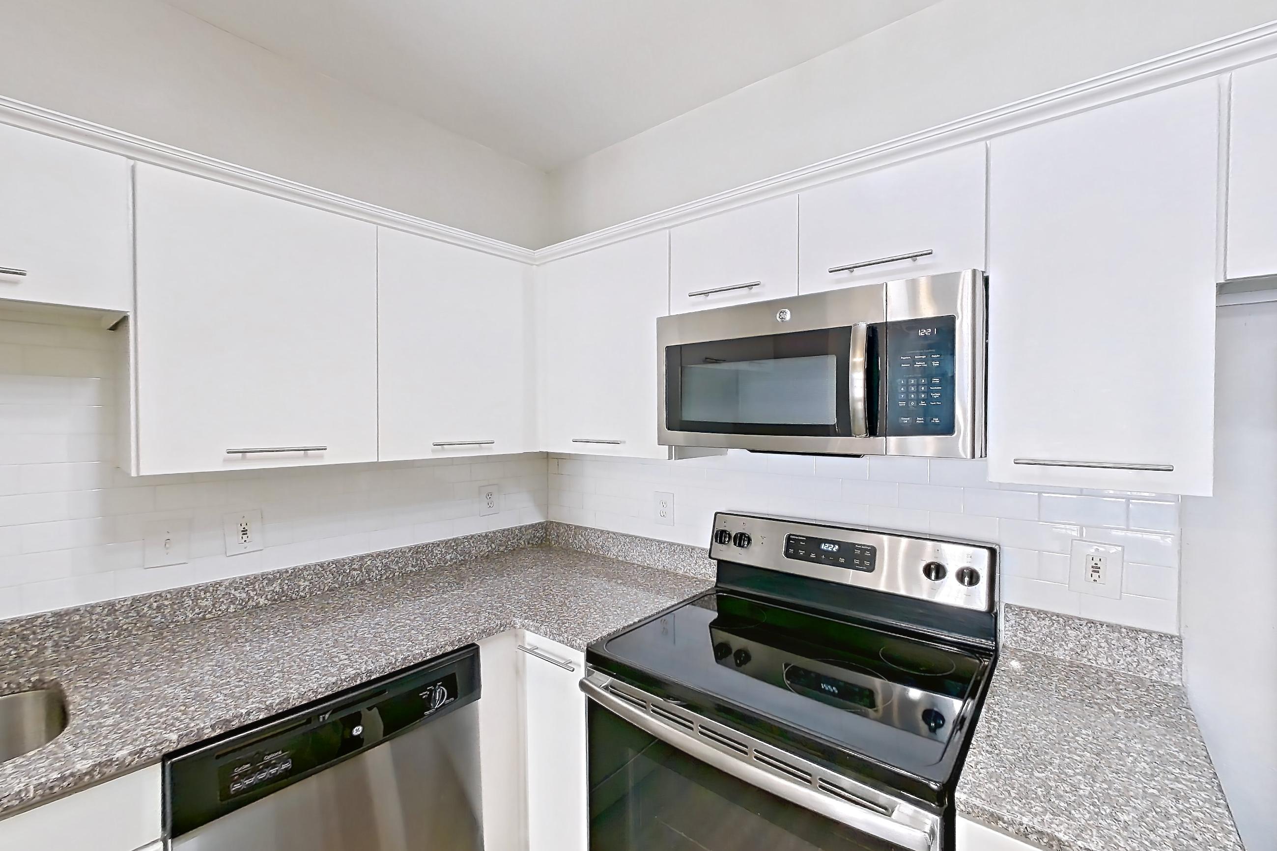 Kitchen with dark wood-finish flooring, dishwasher, electric range, light countertops, light stone countertops, microwave, oven/range, refrigerator, and stainless steel appliances, Apartment 5509 at Marq Perimeter