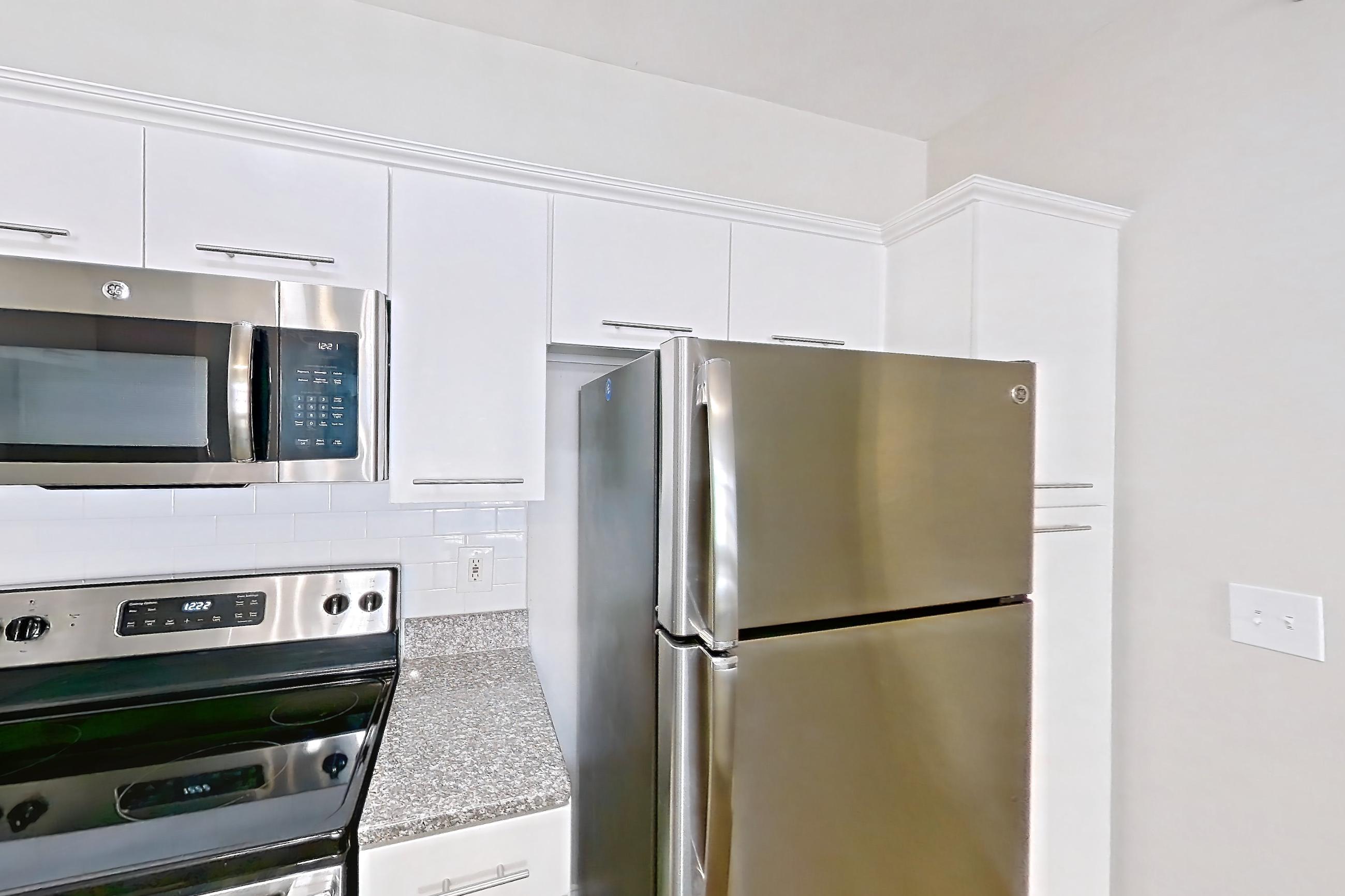 Kitchen with dark wood-finish flooring, dishwasher, electric range, light countertops, light stone countertops, microwave, oven/range, refrigerator, and stainless steel appliances, Apartment 5509 at Marq Perimeter