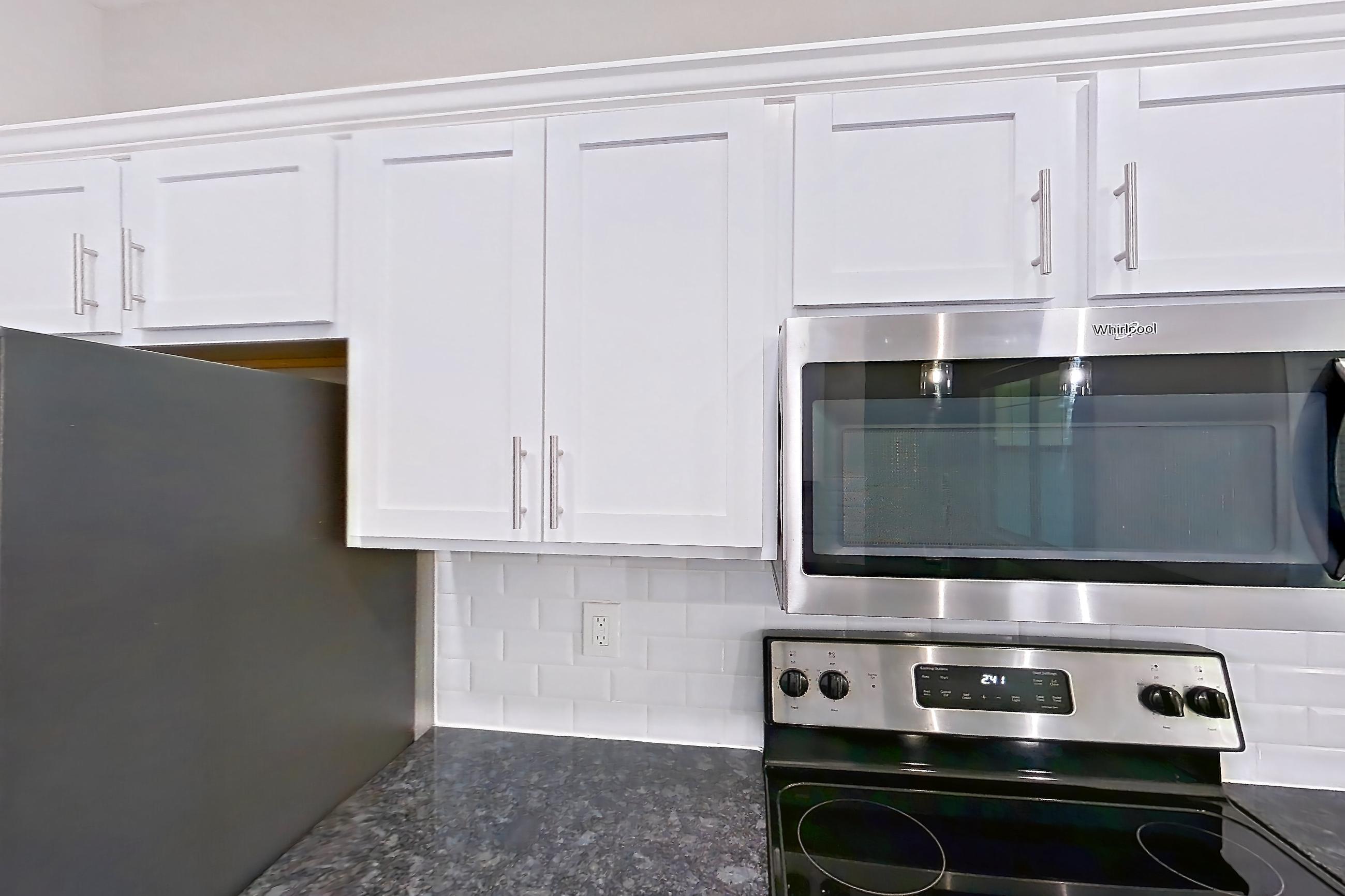 Kitchen with dark stone countertops, dishwasher, electric range, light countertops, light wood-finish flooring, oven/range, refrigerator, and stainless steel appliances, Apartment 5513 at Marq Perimeter
