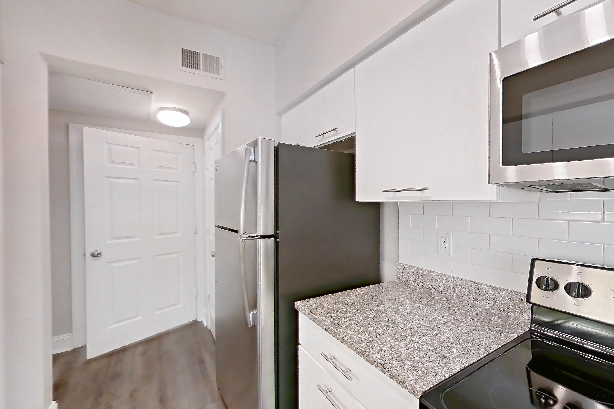Kitchen with dark wood-finish flooring, dishwasher, electric range, light stone countertops, microwave, oven/range, refrigerator, and stainless steel appliances, Apartment 6105 at Marq Perimeter