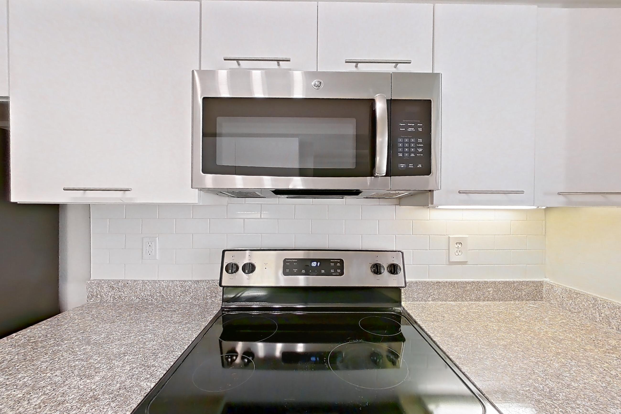 Kitchen with dark wood-finish flooring, dishwasher, electric range, light stone countertops, microwave, oven/range, refrigerator, and stainless steel appliances, Apartment 6105 at Marq Perimeter