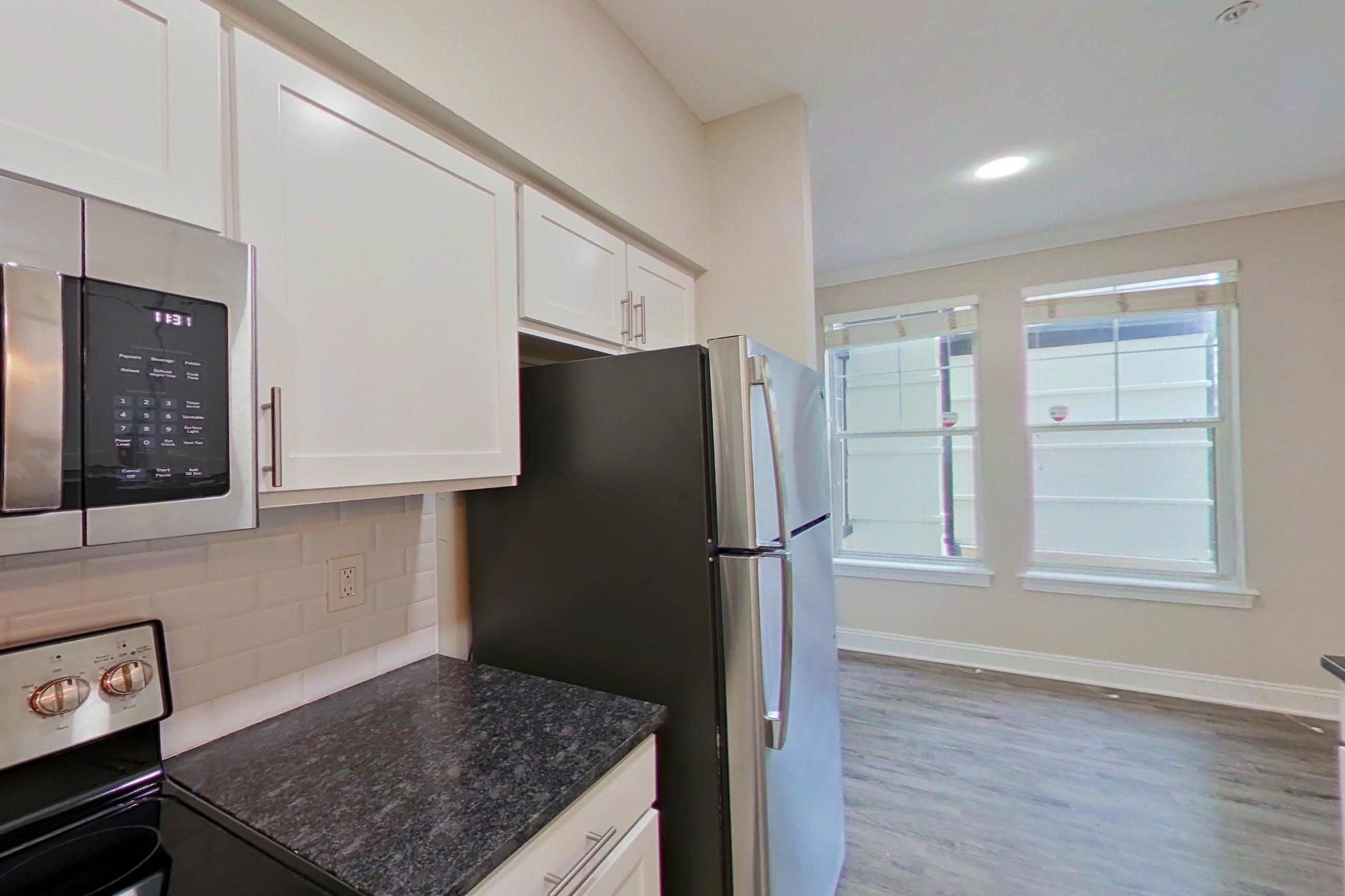 Kitchen with dark stone countertops, electric range, light countertops, light wood-finish flooring, oven/range, refrigerator, and stainless steel appliances, Apartment 6117 at Marq Perimeter