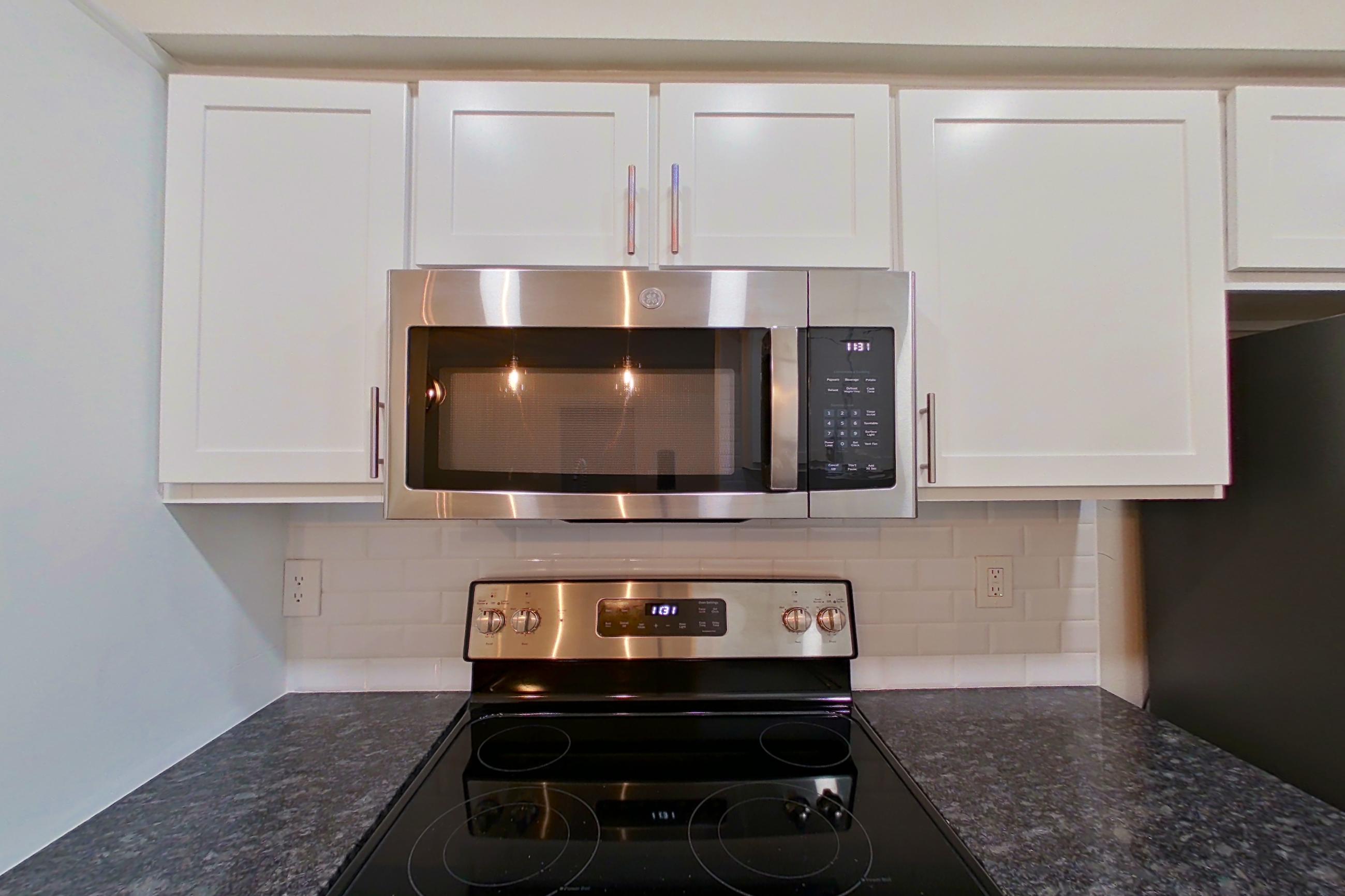 Kitchen with dark stone countertops, electric range, light countertops, light wood-finish flooring, oven/range, refrigerator, and stainless steel appliances, Apartment 6117 at Marq Perimeter