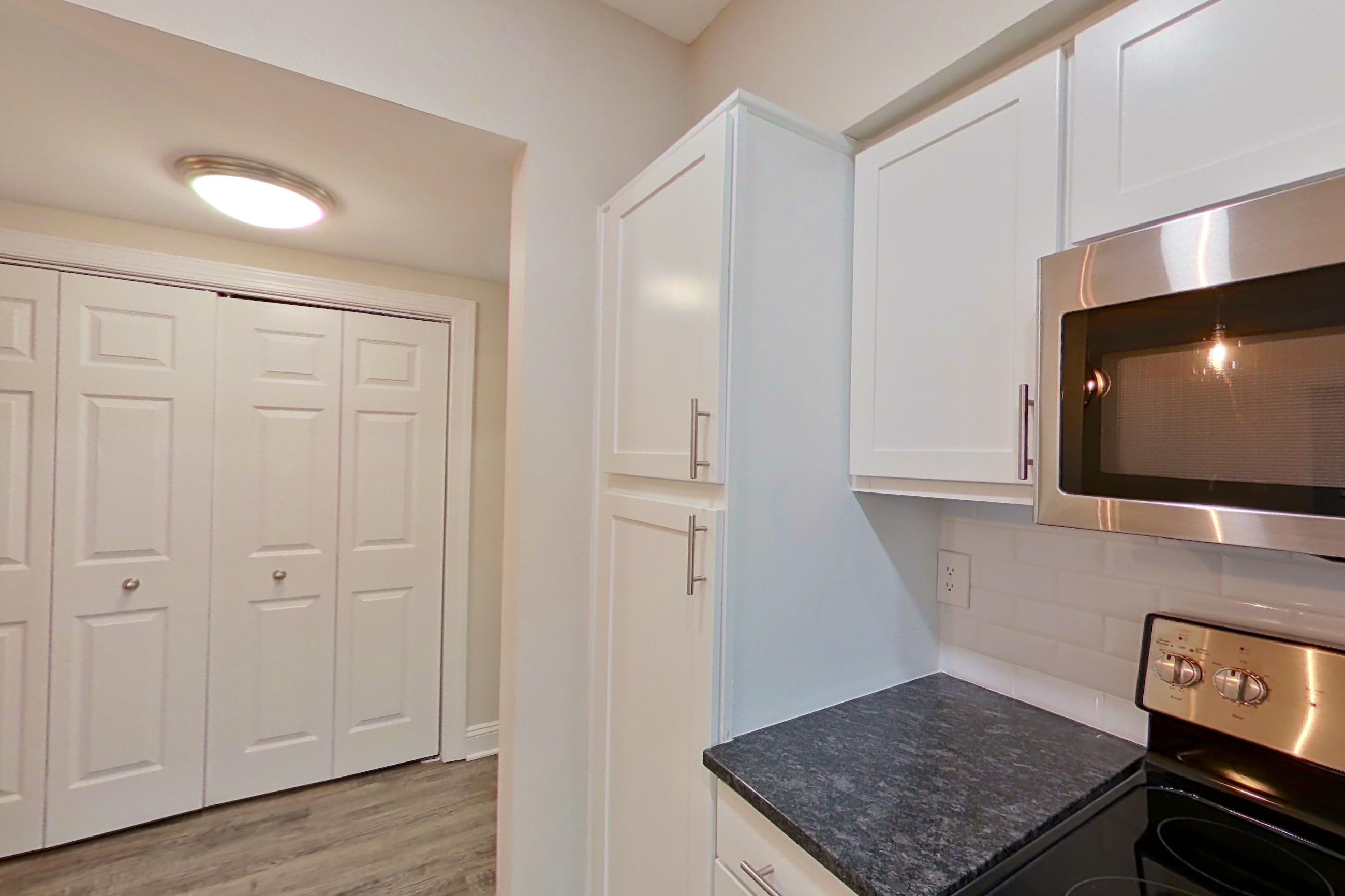 Kitchen with dark stone countertops, electric range, light countertops, light wood-finish flooring, oven/range, refrigerator, and stainless steel appliances, Apartment 6117 at Marq Perimeter
