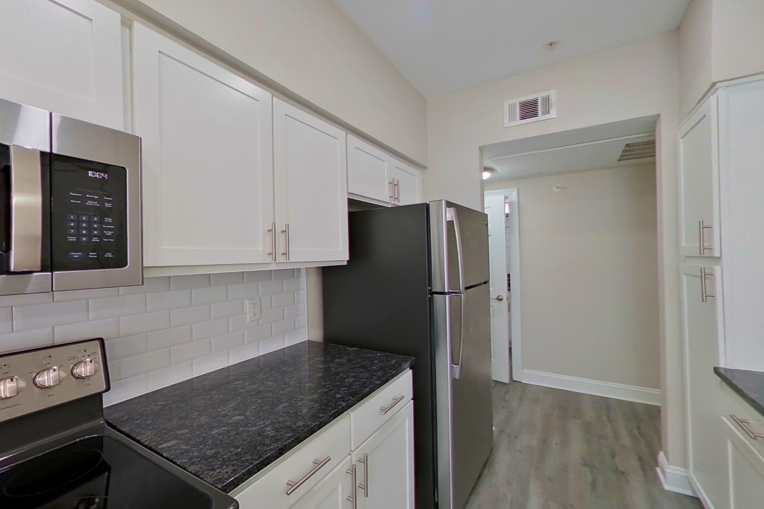 Kitchen with dark stone countertops, electric range, light countertops, light wood-finish flooring, microwave, oven/range, refrigerator, and stainless steel appliances, Apartment 6119 at Marq Perimeter