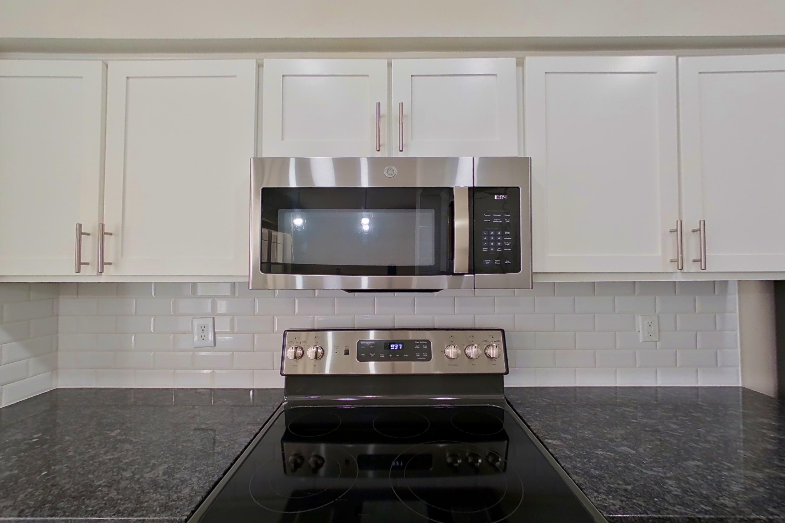 Kitchen with dark stone countertops, electric range, light countertops, light wood-finish flooring, microwave, oven/range, refrigerator, and stainless steel appliances, Apartment 6119 at Marq Perimeter