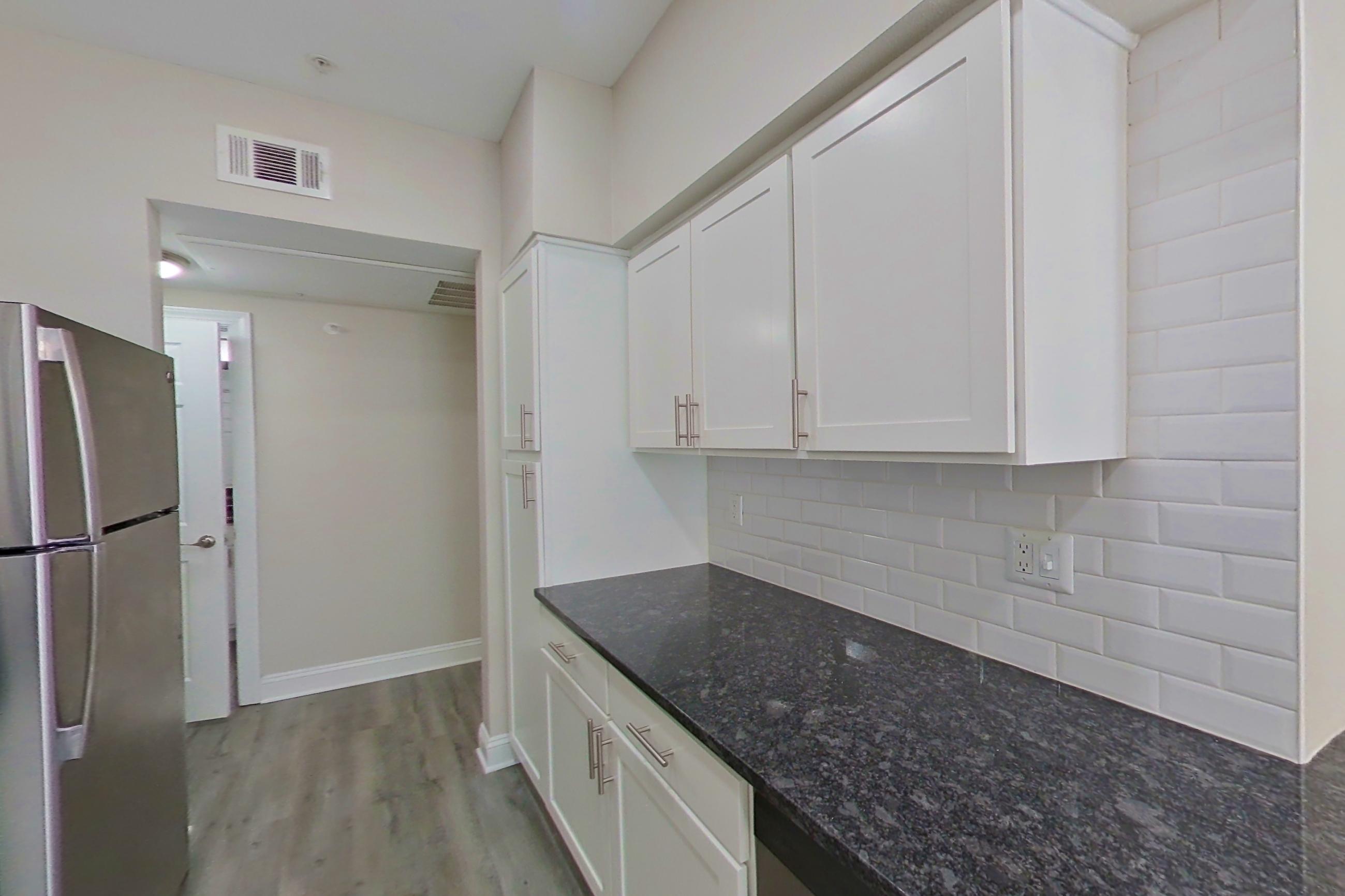 Kitchen with dark stone countertops, electric range, light countertops, light wood-finish flooring, microwave, oven/range, refrigerator, and stainless steel appliances, Apartment 6119 at Marq Perimeter