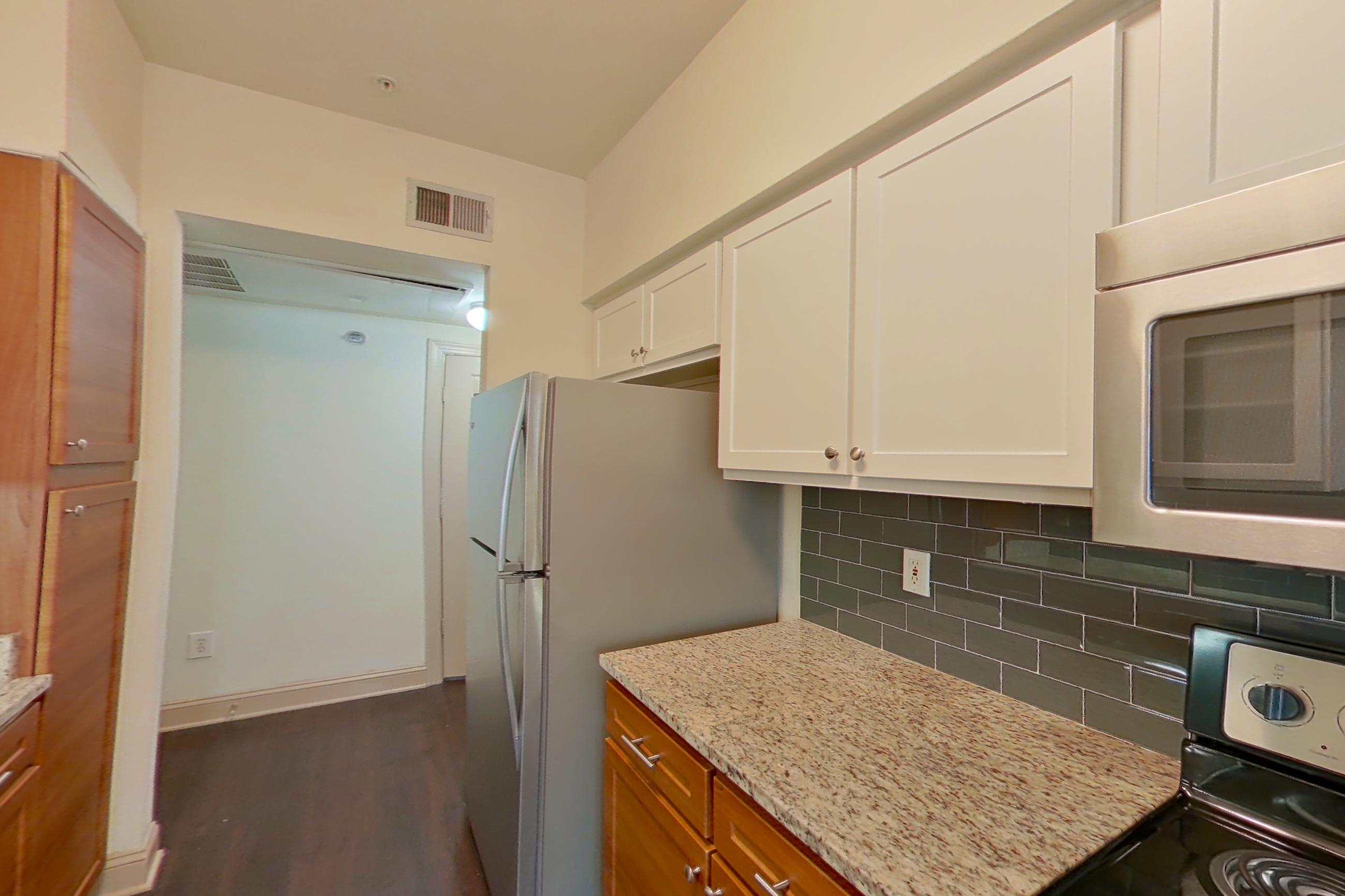 Kitchen with black appliances, dark wood-finish flooring, dishwasher, electric range, light stone countertops, oven/range, and stainless steel appliances, Apartment 6118 at Marq Perimeter