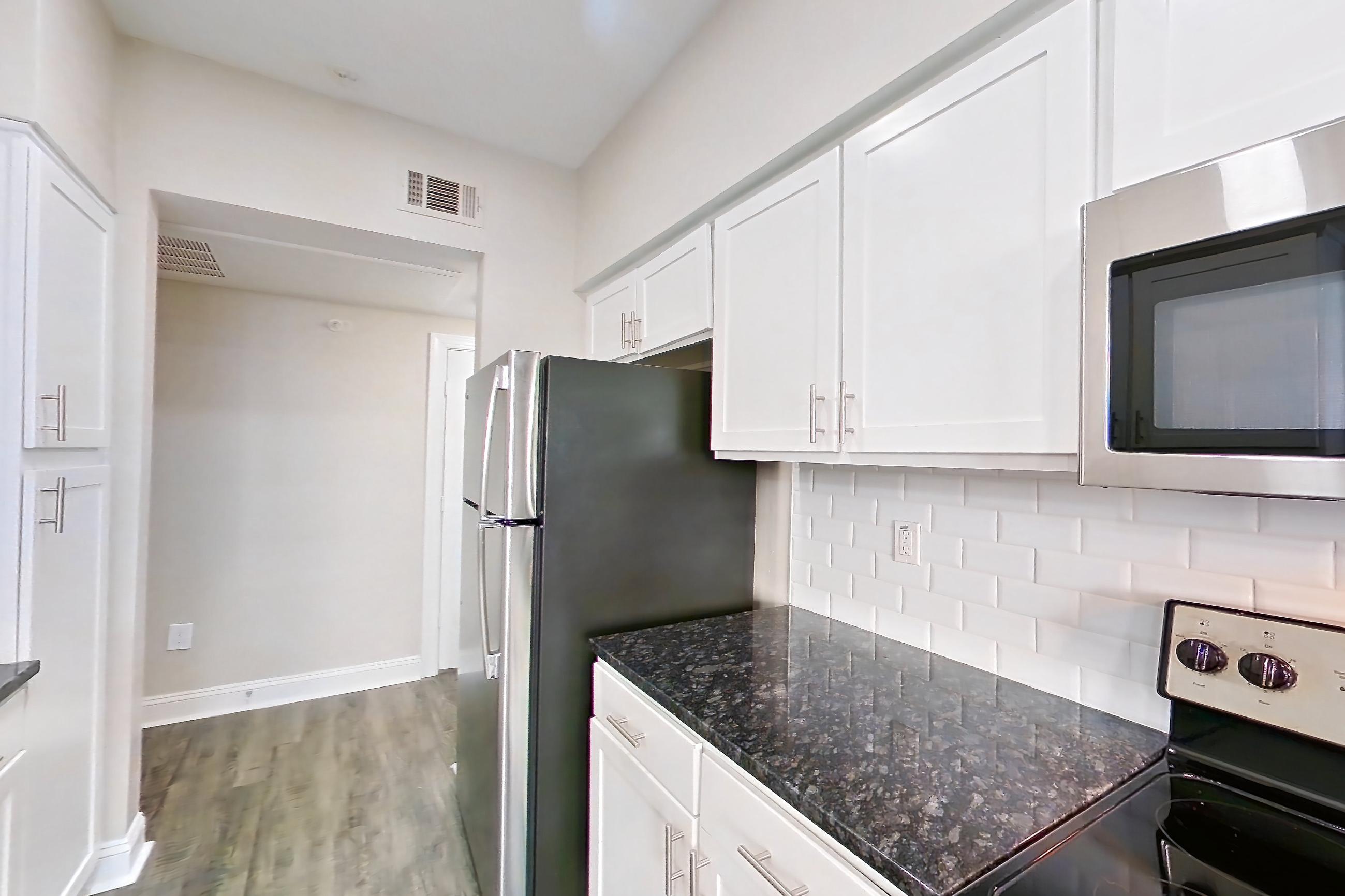 Kitchen with dark stone countertops, dishwasher, electric range, light countertops, light wood-finish flooring, microwave, oven/range, refrigerator, and stainless steel appliances, Apartment 6129 at Marq Perimeter