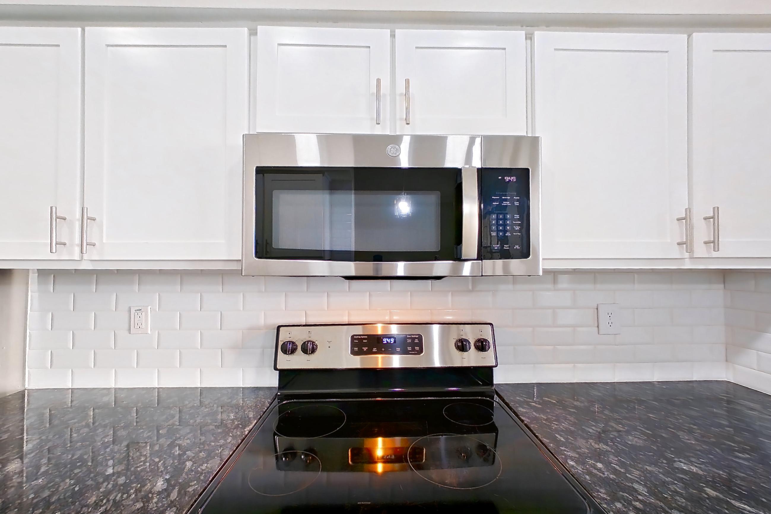 Kitchen with dark stone countertops, dishwasher, electric range, light countertops, light wood-finish flooring, microwave, oven/range, refrigerator, and stainless steel appliances, Apartment 6129 at Marq Perimeter