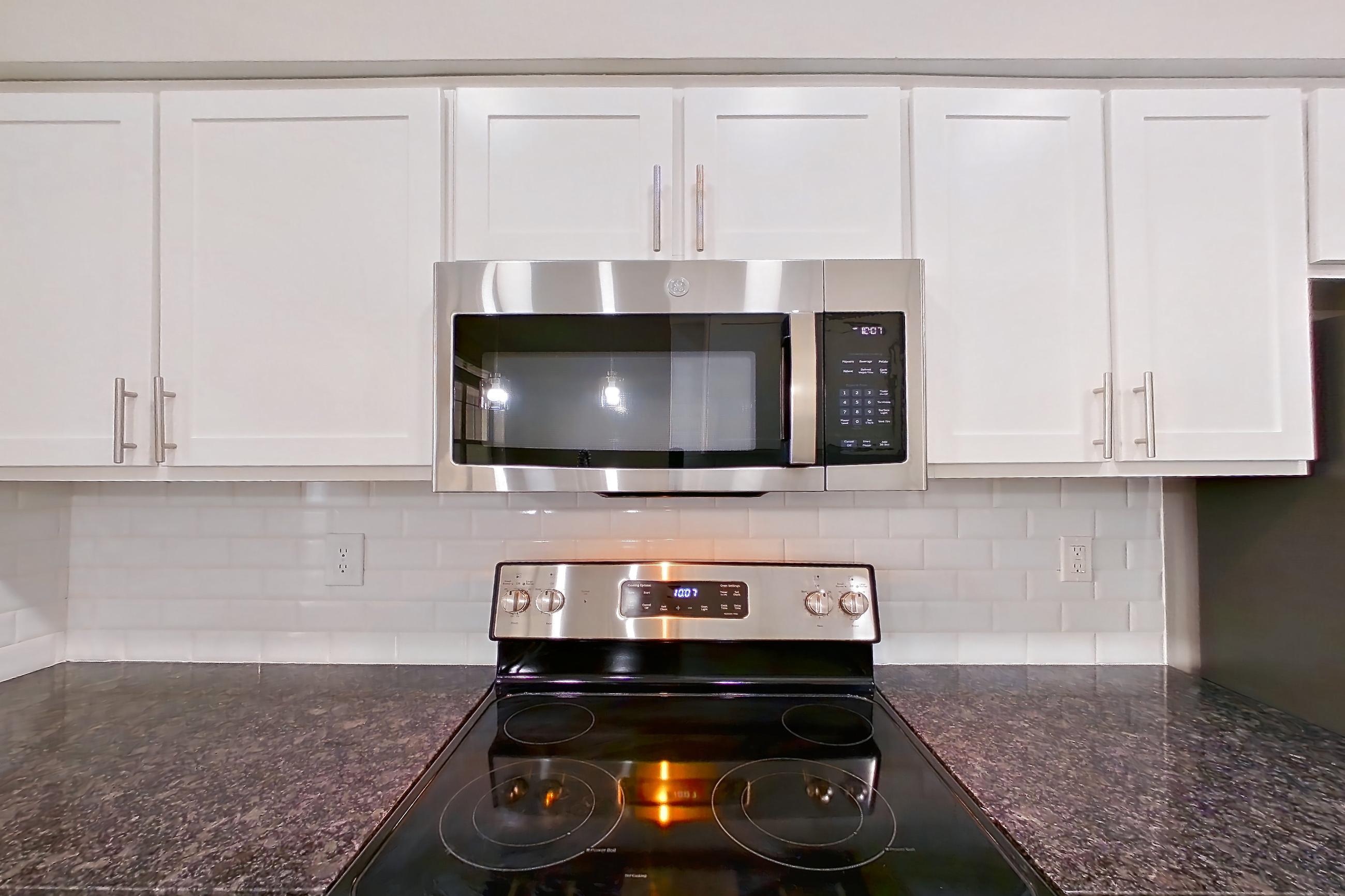 Kitchen with dark stone countertops, dishwasher, electric range, light countertops, oven/range, refrigerator, and stainless steel appliances, Apartment 6131 at Marq Perimeter