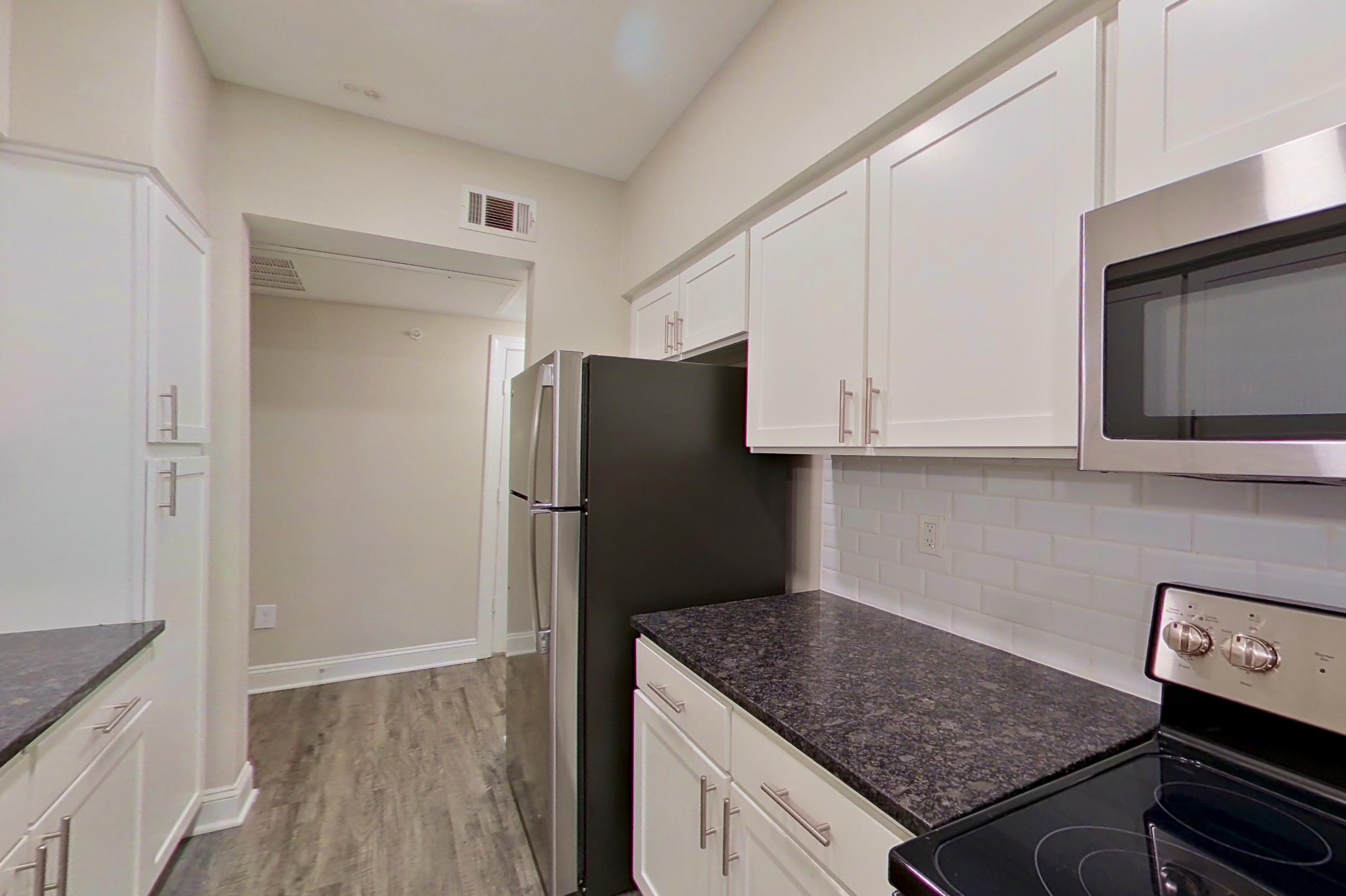 Kitchen with dark stone countertops, dishwasher, electric range, light countertops, light wood-finish flooring, microwave, oven/range, refrigerator, and stainless steel appliances, Apartment 6134 at Marq Perimeter