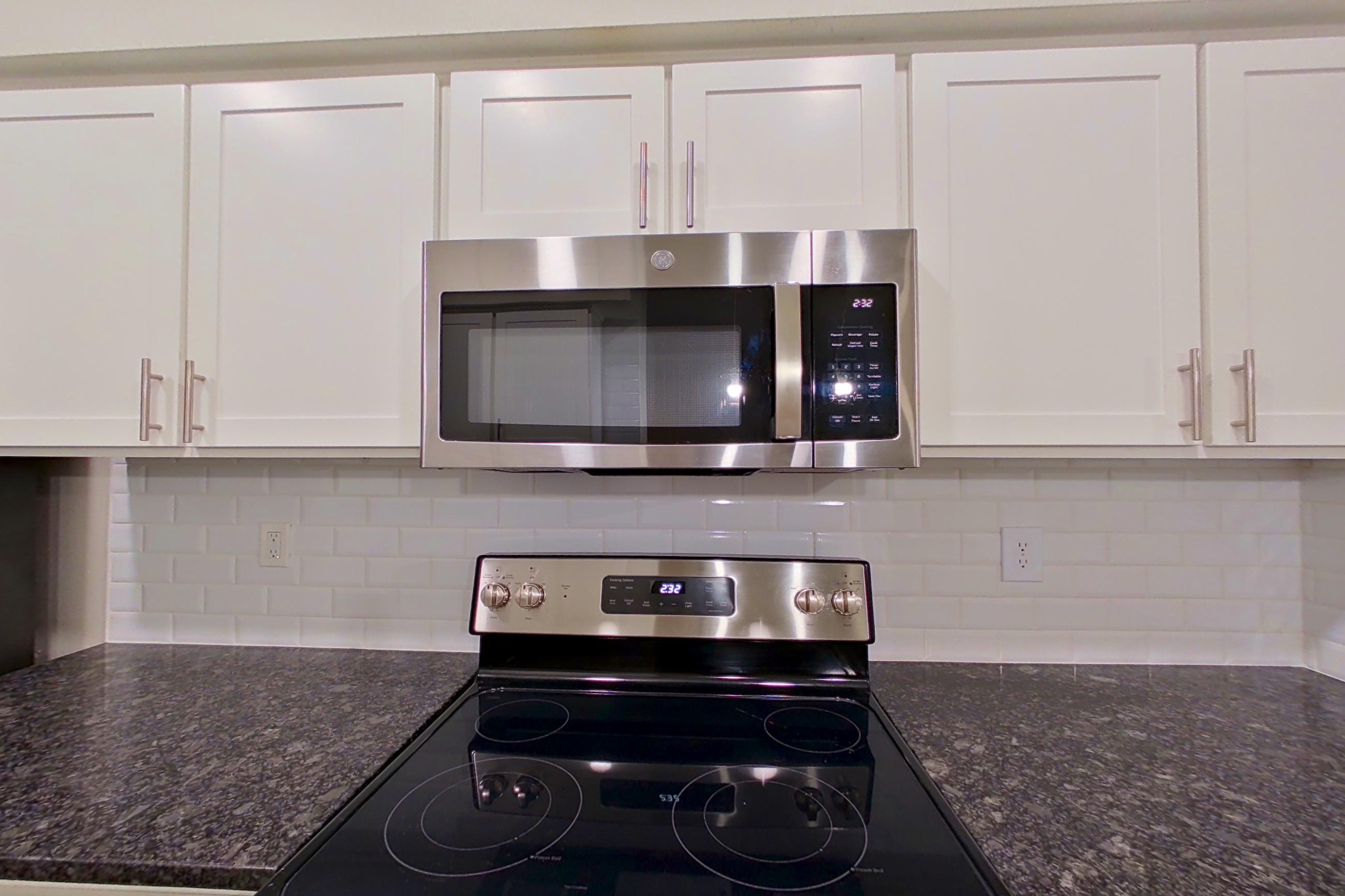 Kitchen with dark stone countertops, dishwasher, electric range, light countertops, light wood-finish flooring, microwave, oven/range, refrigerator, and stainless steel appliances, Apartment 6134 at Marq Perimeter