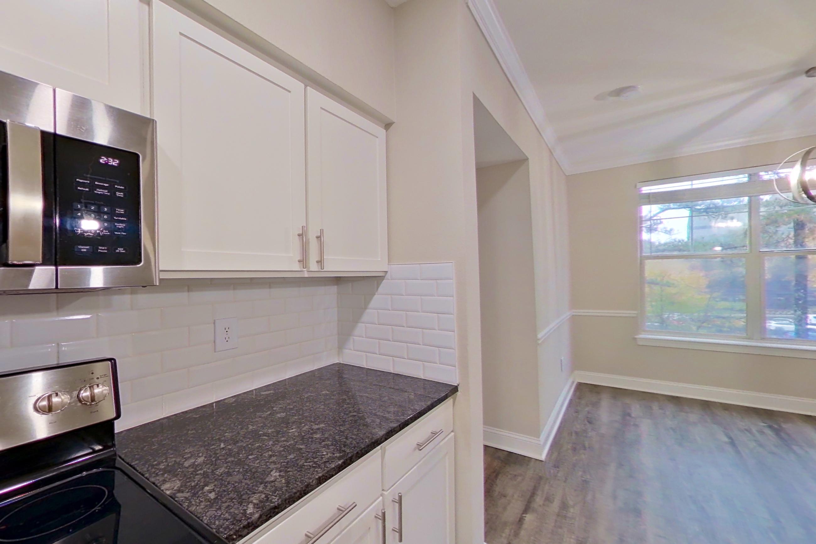 Kitchen with dark stone countertops, dishwasher, electric range, light countertops, light wood-finish flooring, microwave, oven/range, refrigerator, and stainless steel appliances, Apartment 6134 at Marq Perimeter