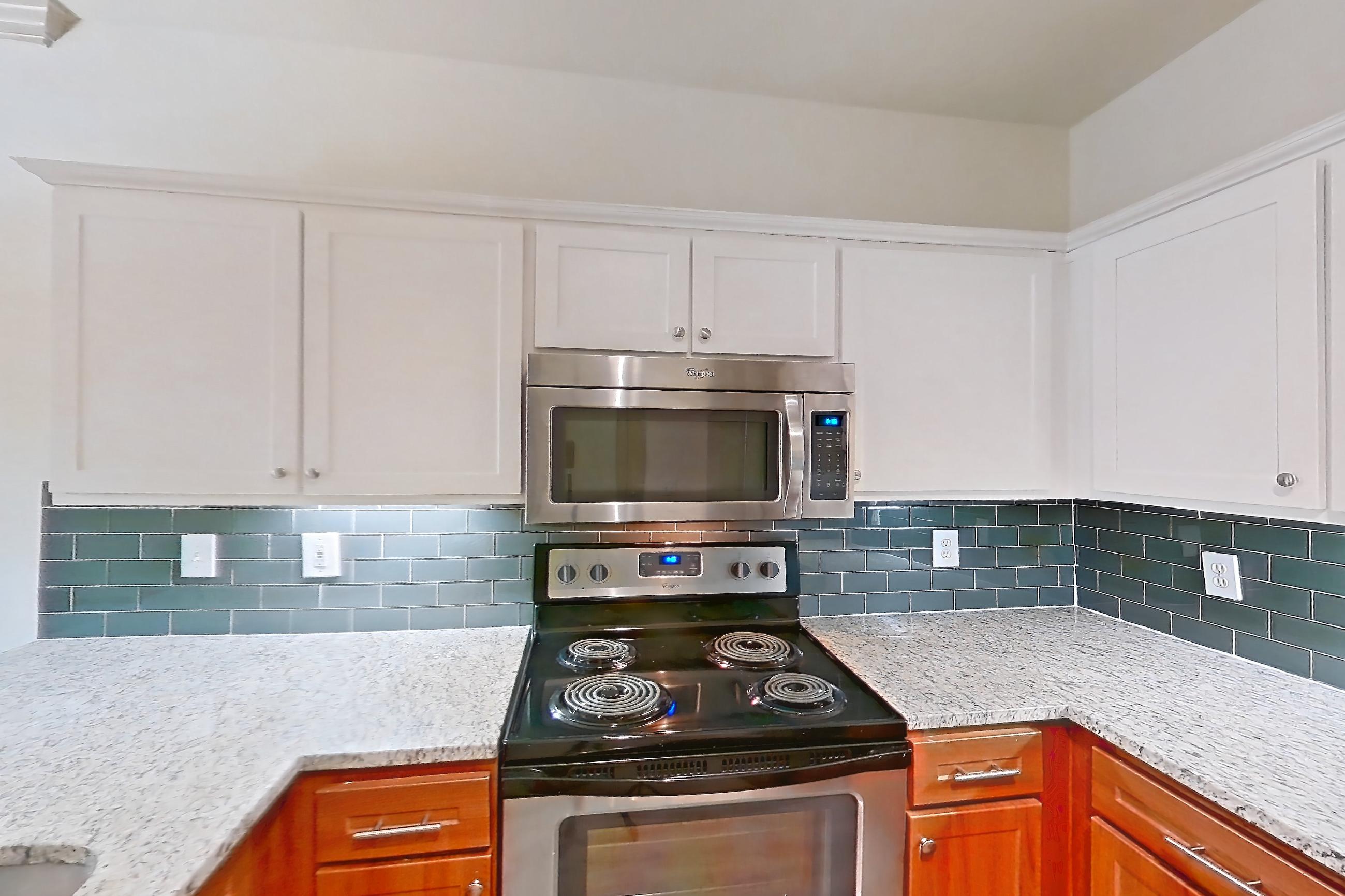 Kitchen with dark wood-finish flooring, dishwasher, electric range, light countertops, light stone countertops, light wood-finish flooring, microwave, oven/range, refrigerator, and stainless steel appliances, Apartment 6203 at Marq Perimeter