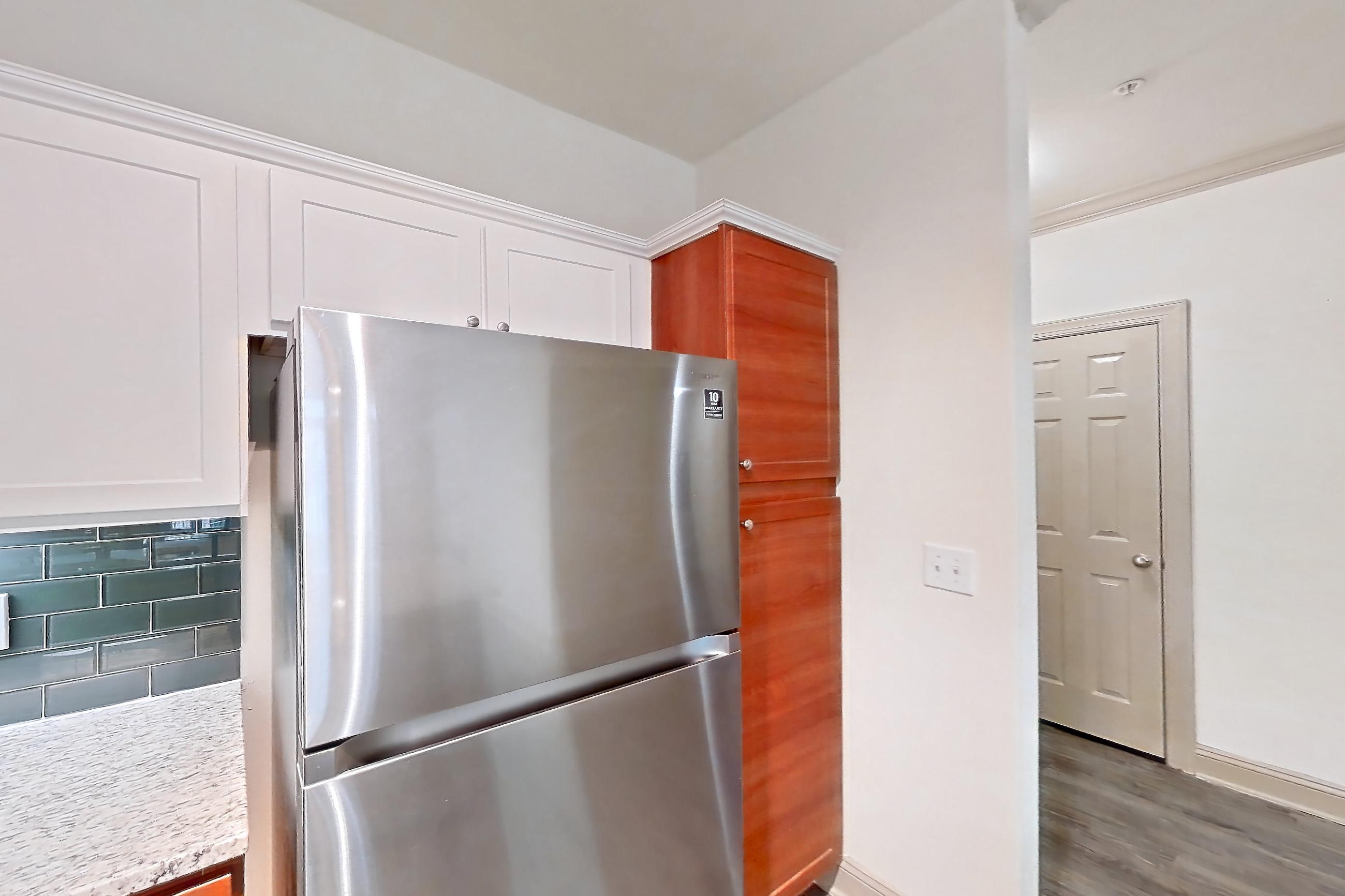 Kitchen with dark wood-finish flooring, dishwasher, electric range, light countertops, light stone countertops, light wood-finish flooring, microwave, oven/range, refrigerator, and stainless steel appliances, Apartment 6203 at Marq Perimeter