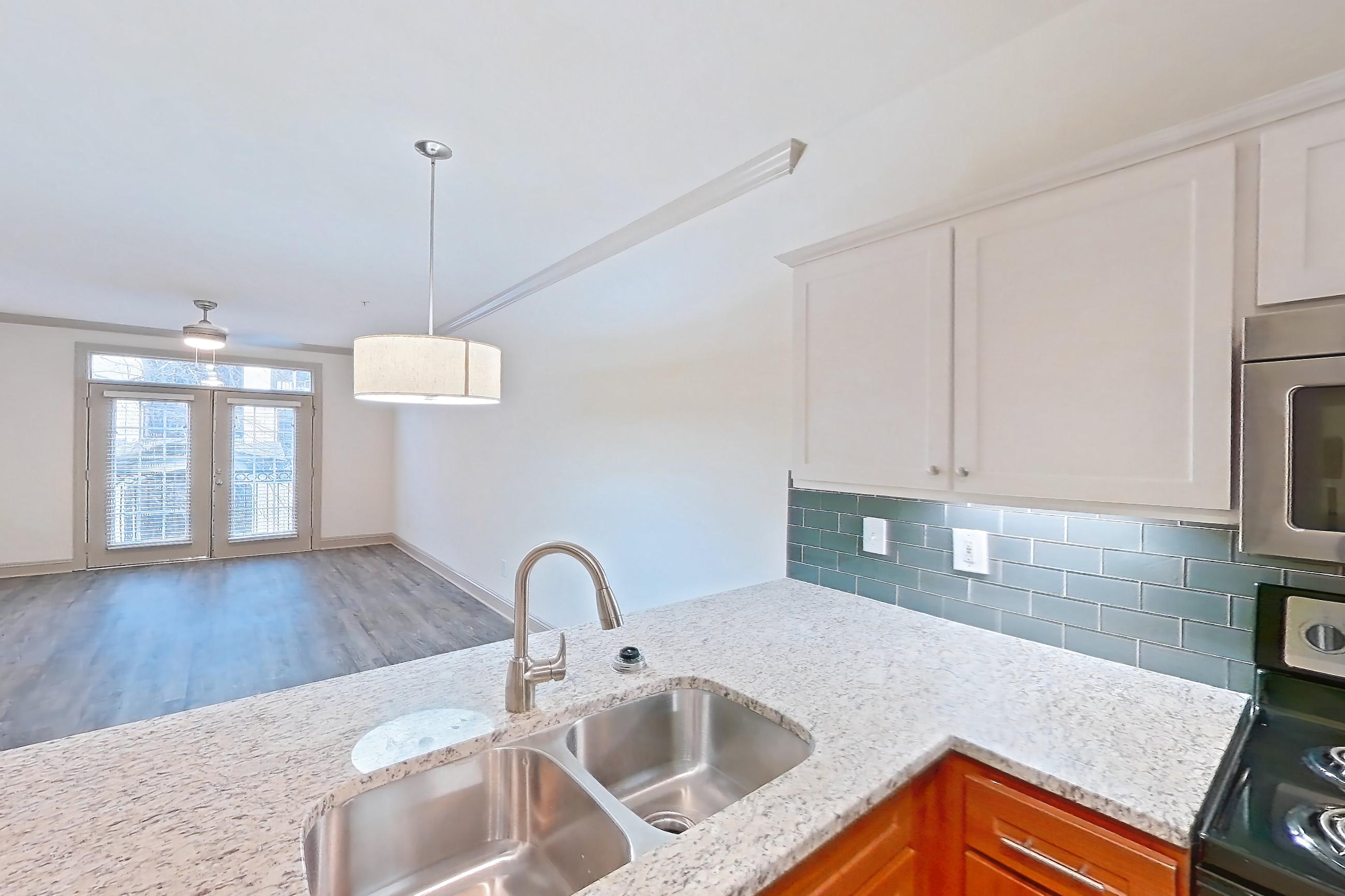 Kitchen with dark wood-finish flooring, dishwasher, electric range, light countertops, light stone countertops, light wood-finish flooring, microwave, oven/range, refrigerator, and stainless steel appliances, Apartment 6203 at Marq Perimeter