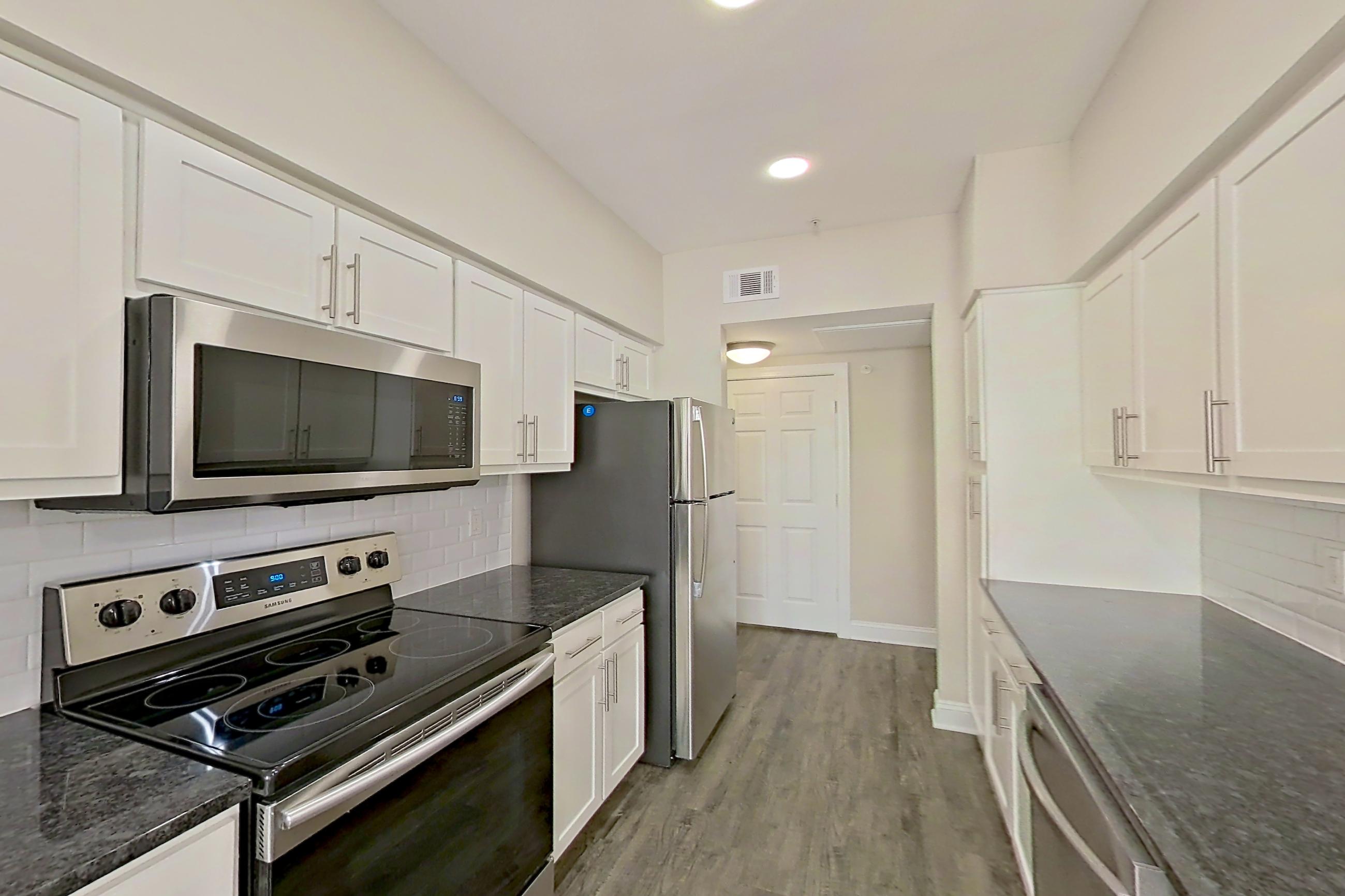 Kitchen with dark stone countertops, dishwasher, electric range, light countertops, light wood-finish flooring, oven/range, and stainless steel appliances, Apartment 6222 at Marq Perimeter
