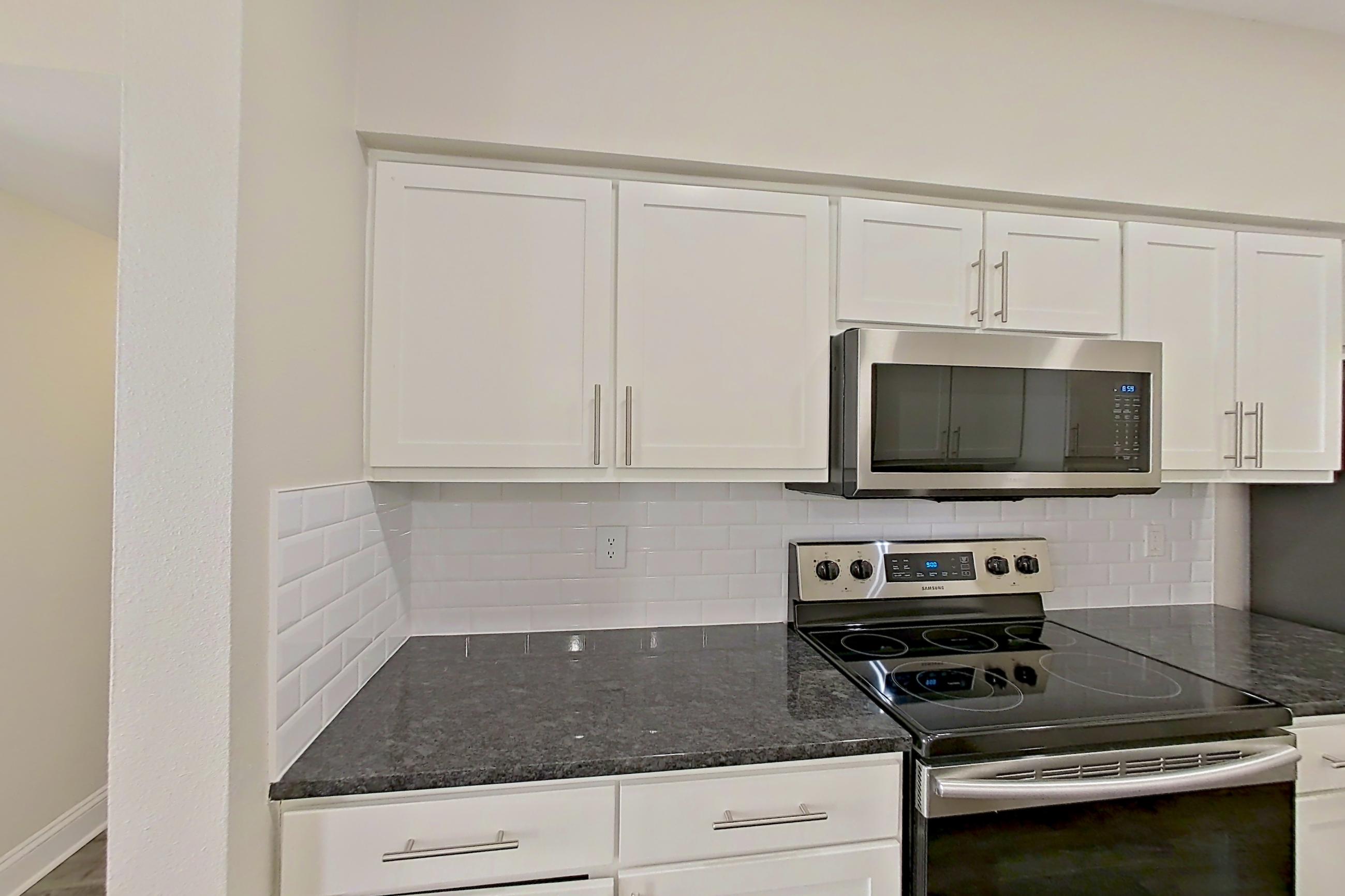Kitchen with dark stone countertops, dishwasher, electric range, light countertops, light wood-finish flooring, oven/range, and stainless steel appliances, Apartment 6222 at Marq Perimeter