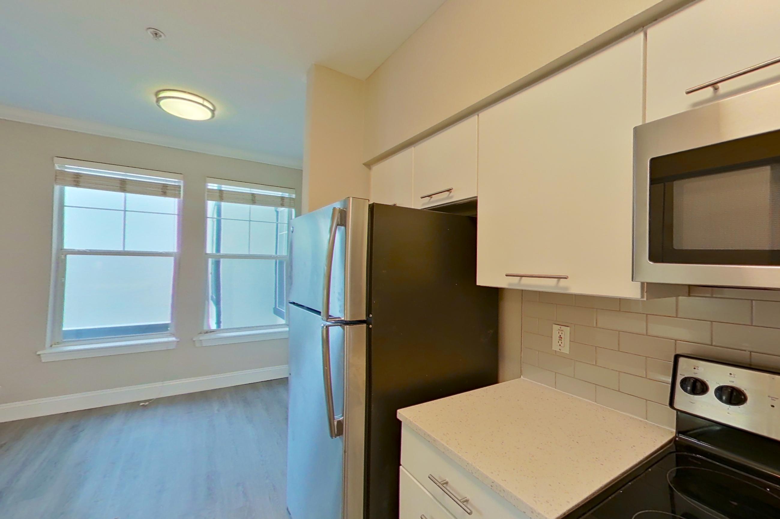 Kitchen with dishwasher, electric range, light stone countertops, light vinyl flooring, light wood-finish flooring, microwave, oven/range, refrigerator, and stainless steel appliances, Apartment 6235 at Marq Perimeter
