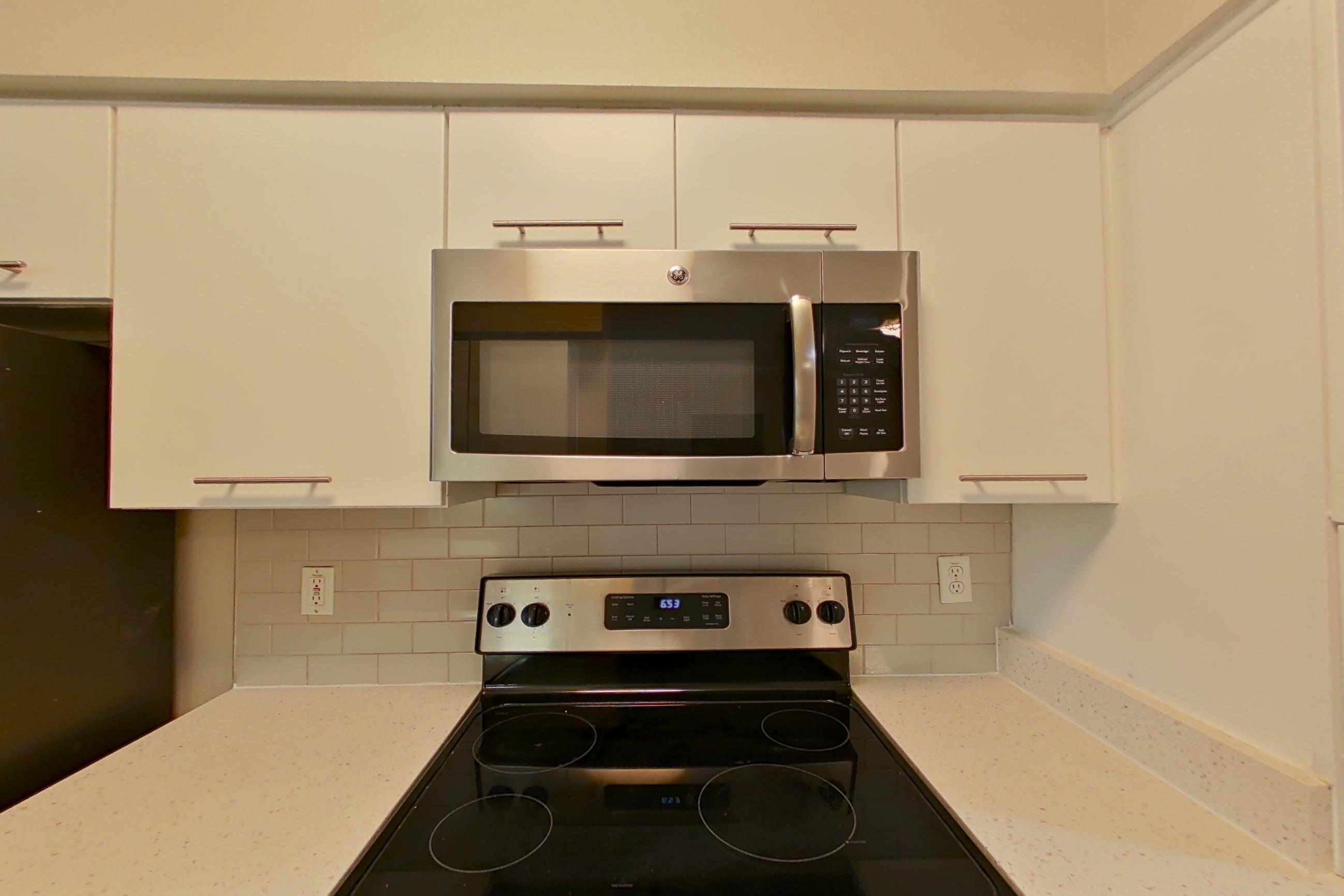 Kitchen with dishwasher, electric range, light stone countertops, light vinyl flooring, light wood-finish flooring, microwave, oven/range, refrigerator, and stainless steel appliances, Apartment 6235 at Marq Perimeter