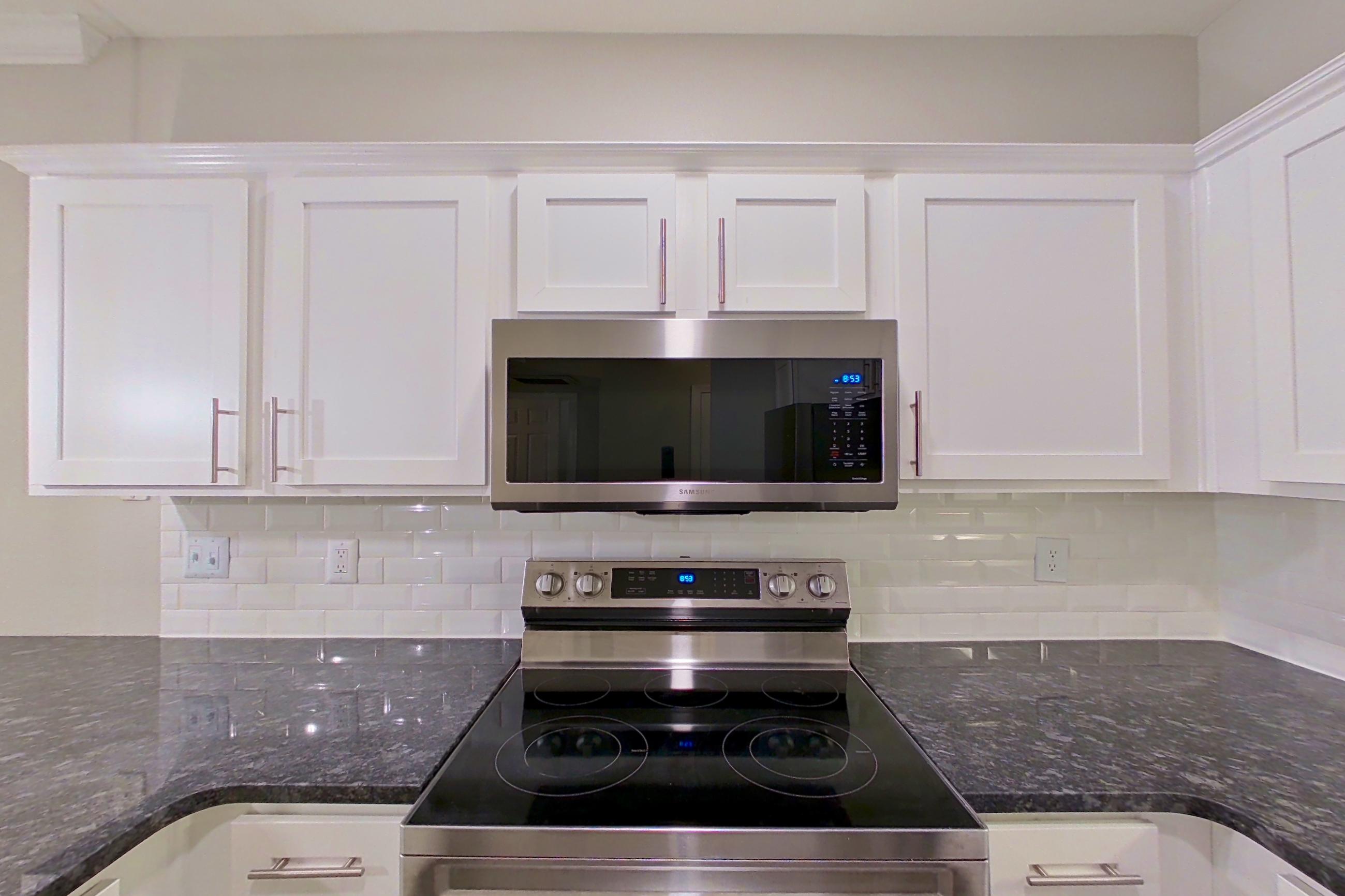 Kitchen with dark stone countertops, dishwasher, electric range, light countertops, microwave, oven/range, refrigerator, and stainless steel appliances, Apartment 6303 at Marq Perimeter
