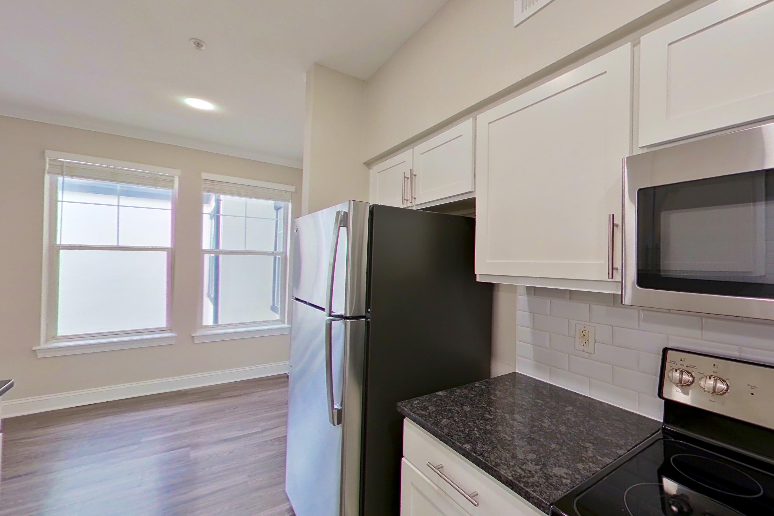 Kitchen with dark stone countertops, dark wood-finish flooring, dishwasher, electric range, light countertops, microwave, oven/range, refrigerator, and stainless steel appliances, Apartment 6313 at Marq Perimeter