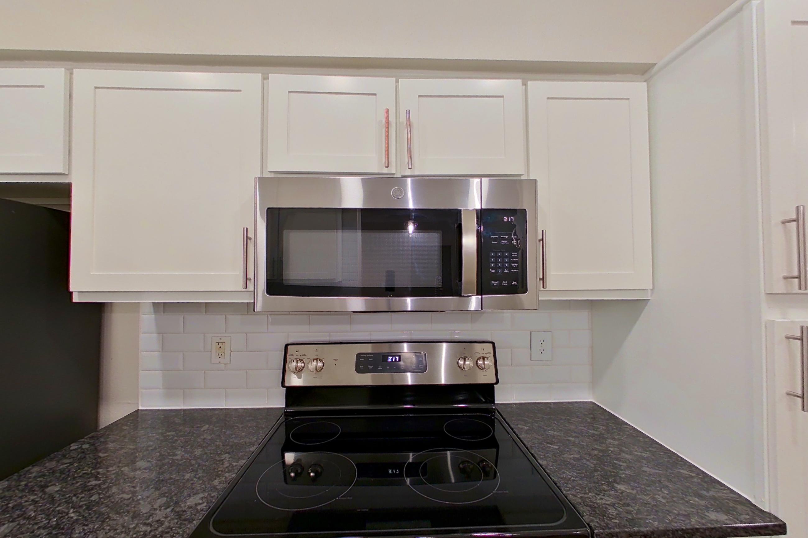 Kitchen with dark stone countertops, dark wood-finish flooring, dishwasher, electric range, light countertops, microwave, oven/range, refrigerator, and stainless steel appliances, Apartment 6313 at Marq Perimeter