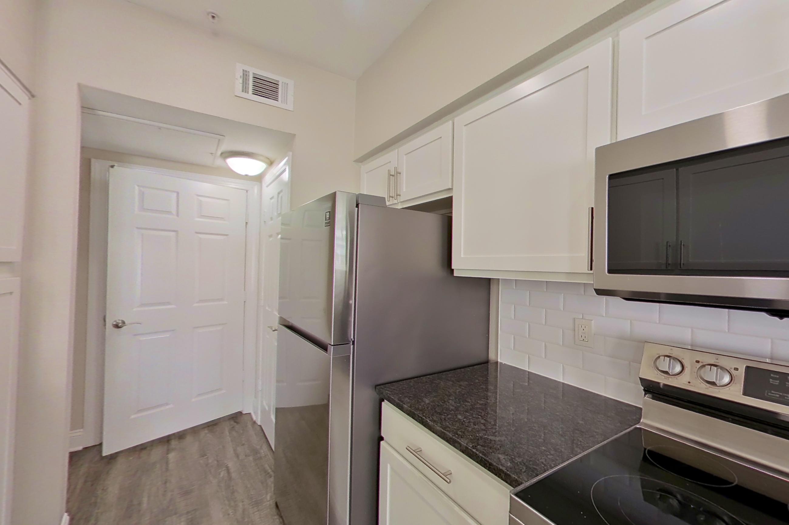 Kitchen with dark stone countertops, dark wood-finish flooring, dishwasher, electric range, light countertops, light wood-finish flooring, oven/range, refrigerator, and stainless steel appliances, Apartment 6320 at Marq Perimeter