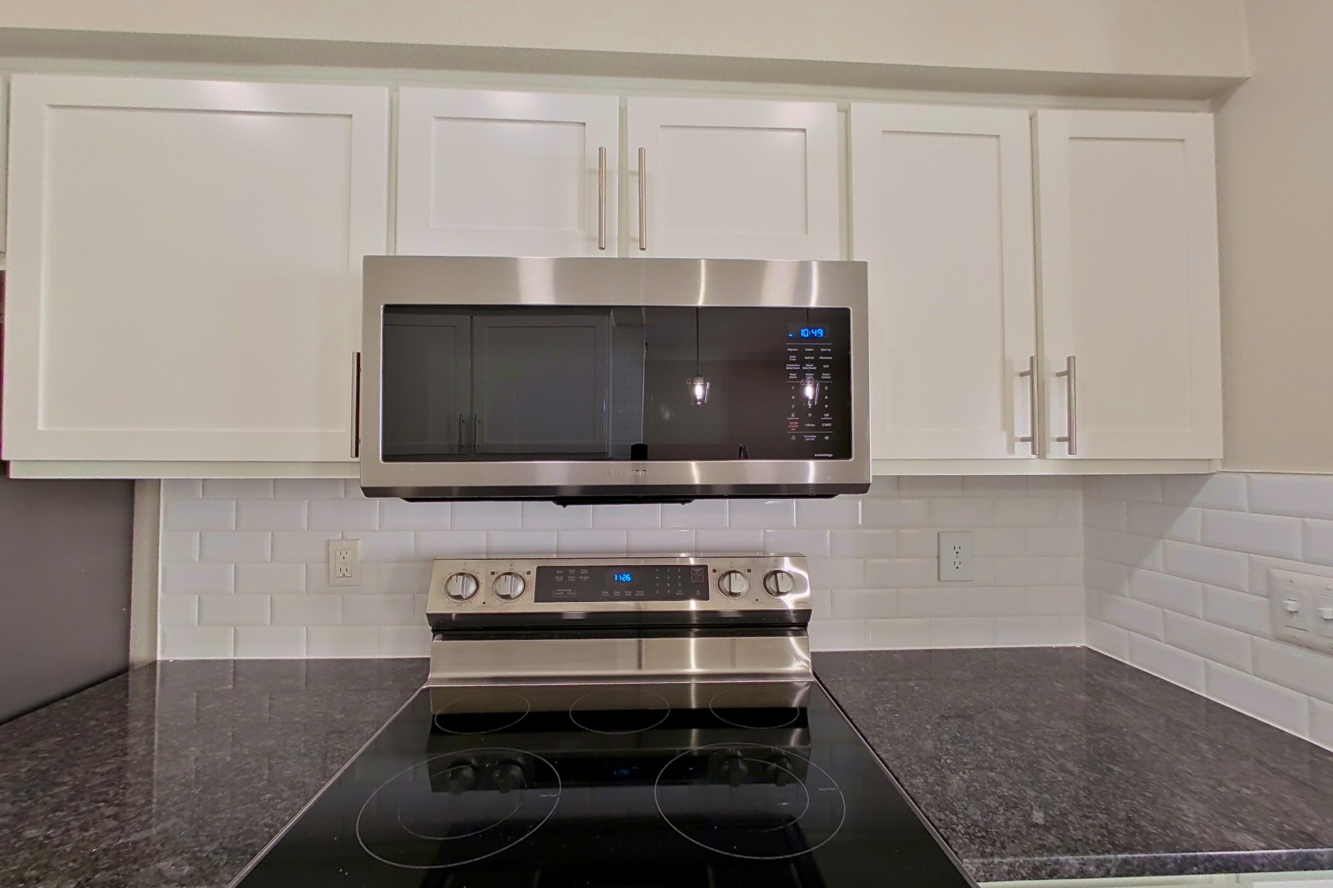 Kitchen with dark stone countertops, dark wood-finish flooring, dishwasher, electric range, light countertops, light wood-finish flooring, oven/range, refrigerator, and stainless steel appliances, Apartment 6320 at Marq Perimeter