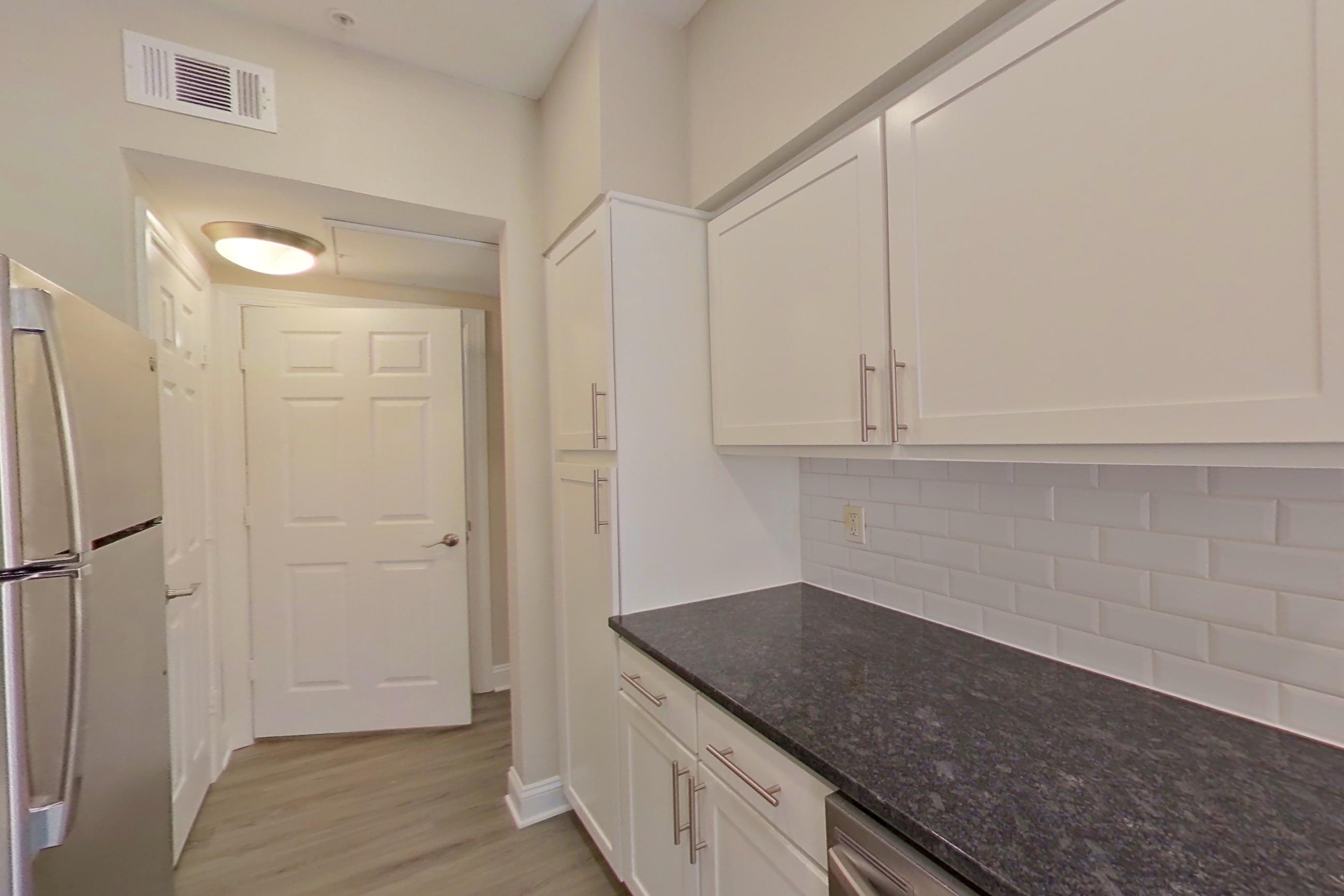 Kitchen with dark stone countertops, dishwasher, electric range, light countertops, light wood-finish flooring, oven/range, refrigerator, and stainless steel appliances, Apartment 6321 at Marq Perimeter