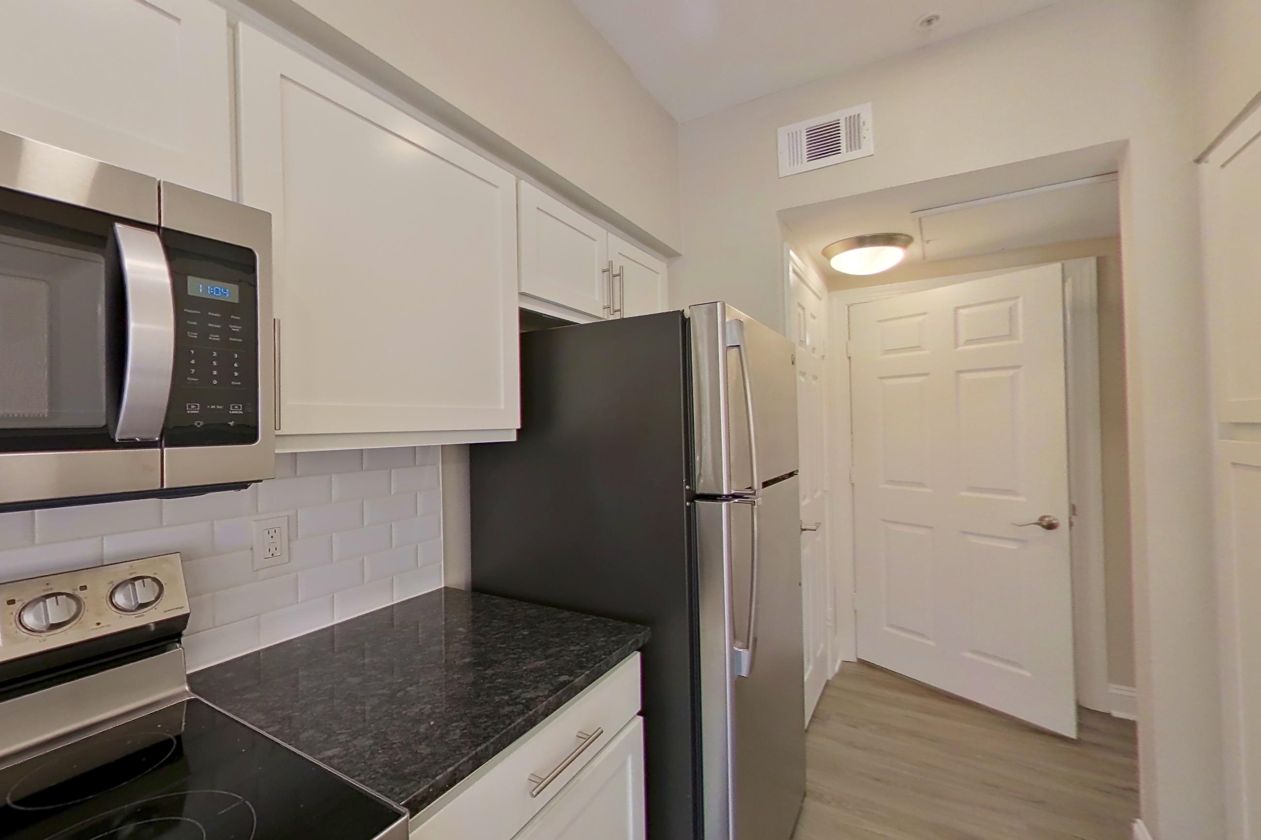 Kitchen with dark stone countertops, dishwasher, electric range, light countertops, light wood-finish flooring, oven/range, refrigerator, and stainless steel appliances, Apartment 6321 at Marq Perimeter