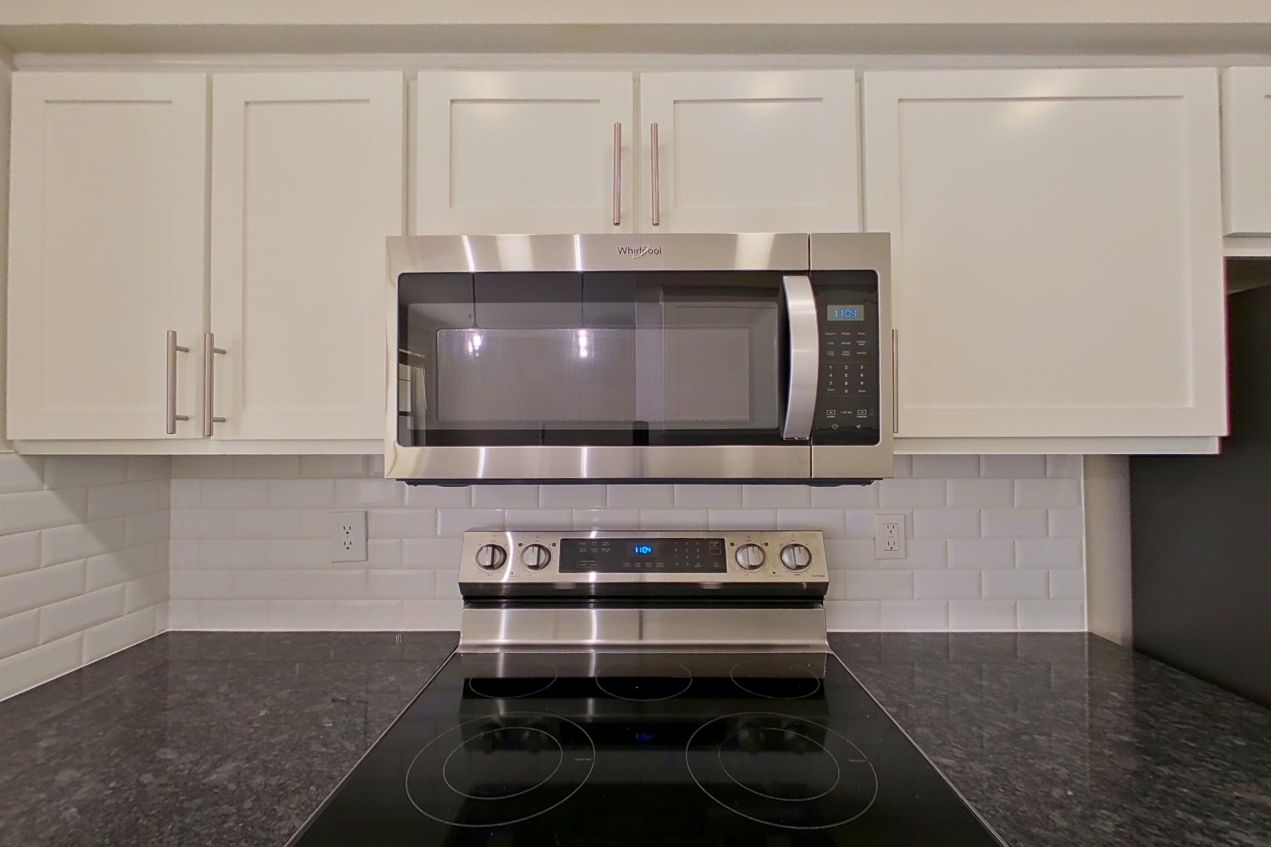 Kitchen with dark stone countertops, dishwasher, electric range, light countertops, light wood-finish flooring, oven/range, refrigerator, and stainless steel appliances, Apartment 6321 at Marq Perimeter