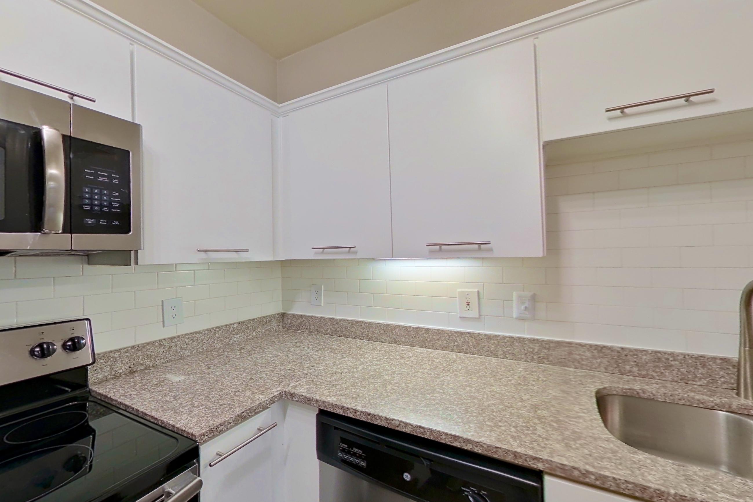 Kitchen with dishwasher, electric range, light countertops, light stone countertops, microwave, oven/range, refrigerator, and stainless steel appliances, Apartment 6324 at Marq Perimeter