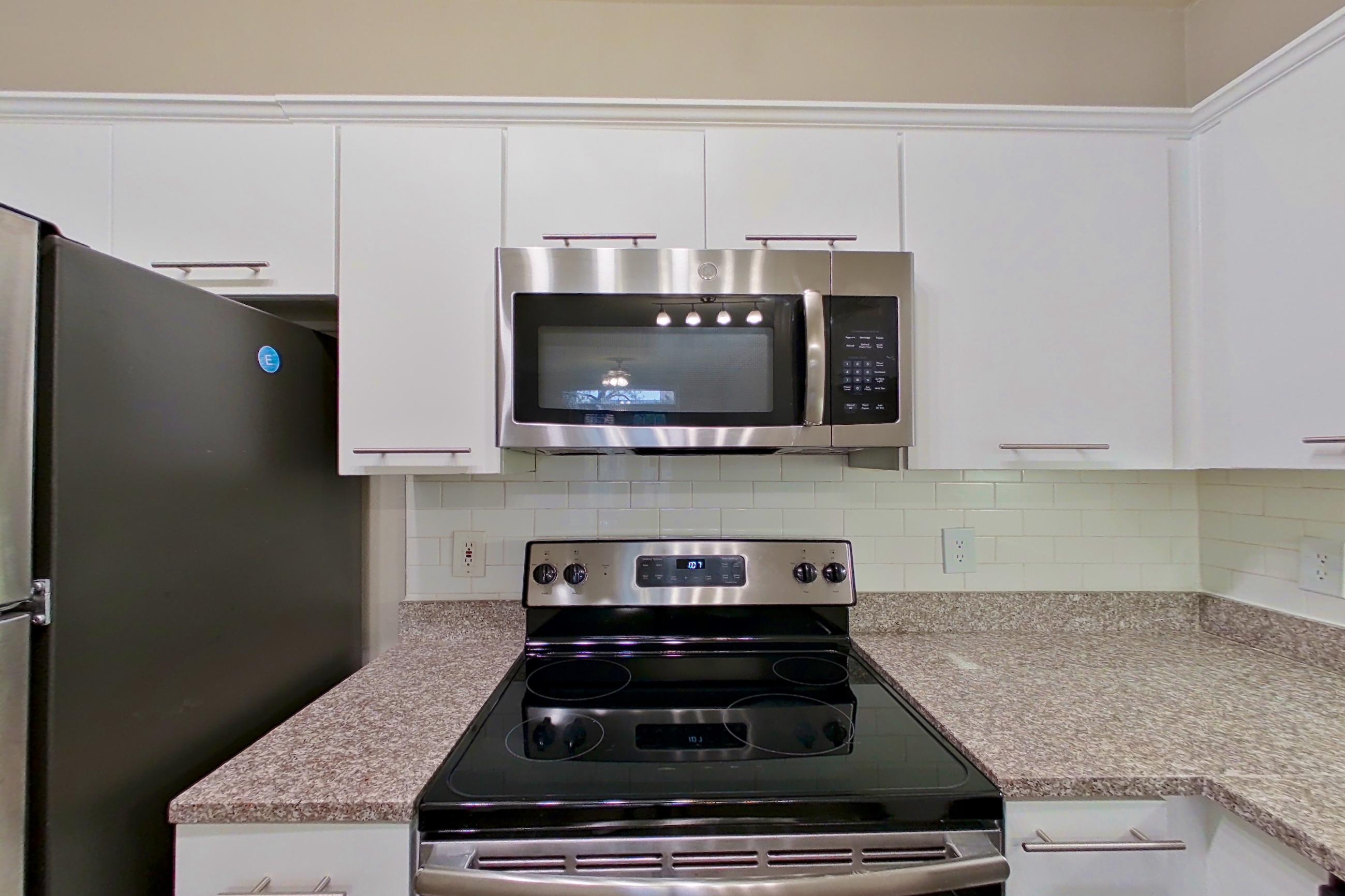 Kitchen with dishwasher, electric range, light countertops, light stone countertops, microwave, oven/range, refrigerator, and stainless steel appliances, Apartment 6324 at Marq Perimeter