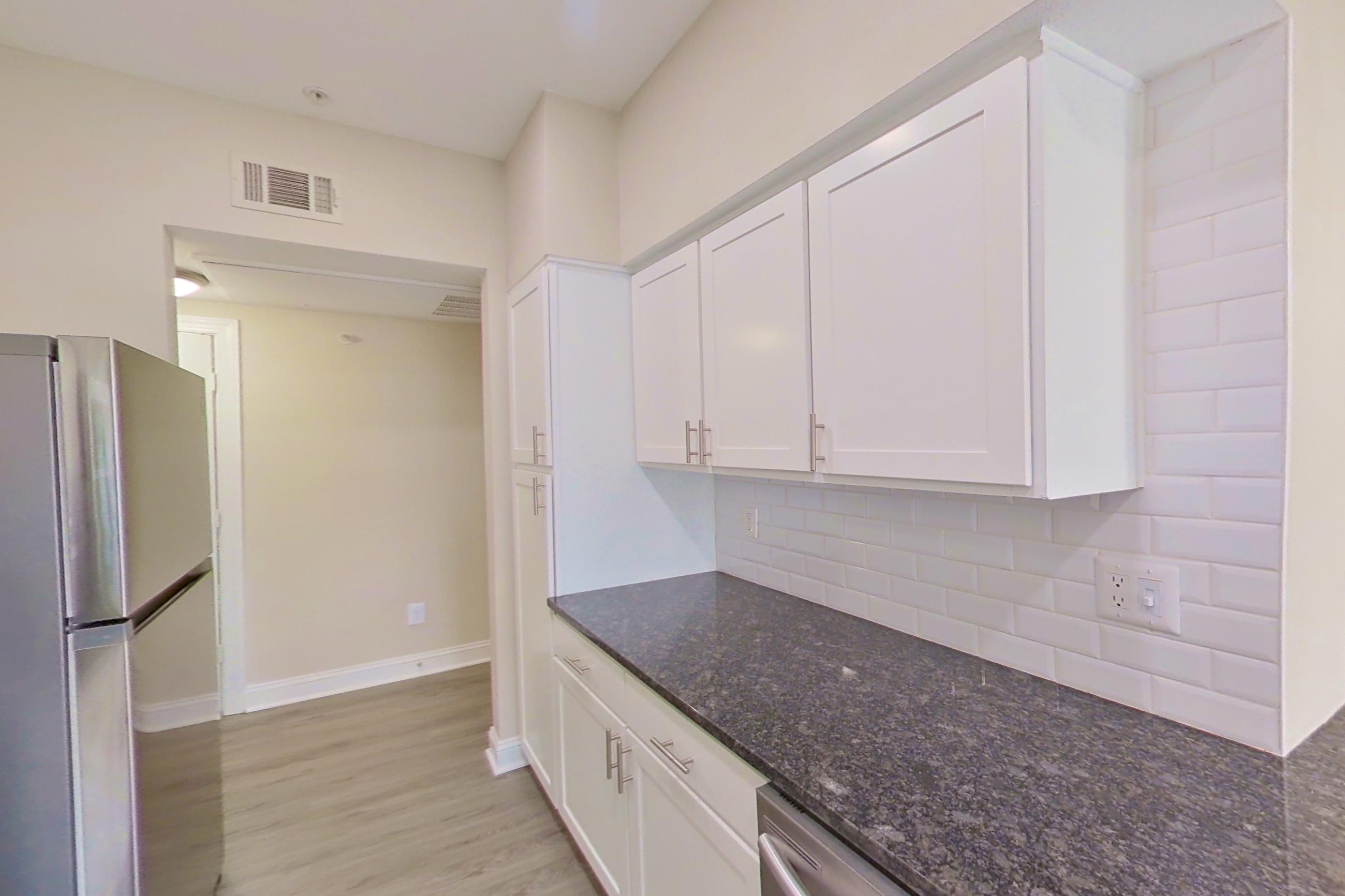 Kitchen with dark stone countertops, dishwasher, electric range, light countertops, light wood-finish flooring, microwave, oven/range, refrigerator, and stainless steel appliances, Apartment 6325 at Marq Perimeter