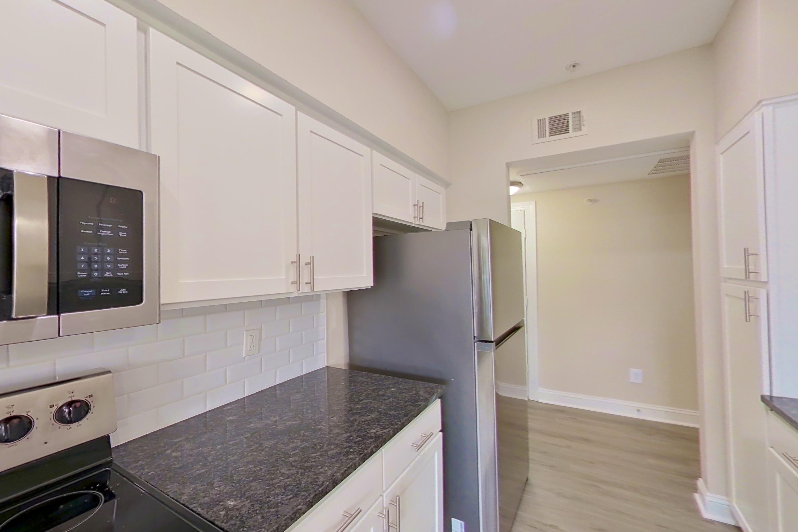Kitchen with dark stone countertops, dishwasher, electric range, light countertops, light wood-finish flooring, microwave, oven/range, refrigerator, and stainless steel appliances, Apartment 6325 at Marq Perimeter