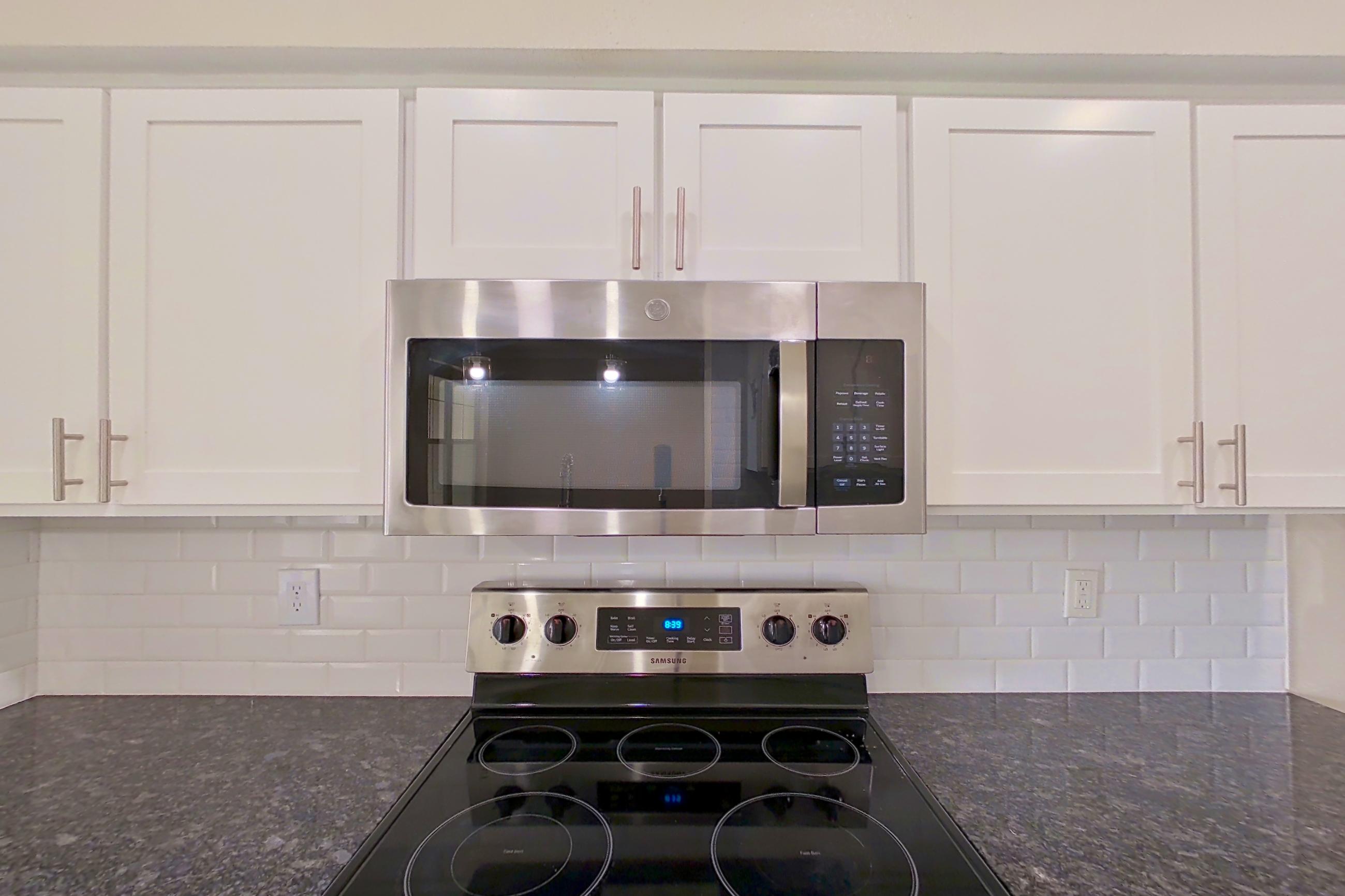 Kitchen with dark stone countertops, dishwasher, electric range, light countertops, light wood-finish flooring, microwave, oven/range, refrigerator, and stainless steel appliances, Apartment 6325 at Marq Perimeter
