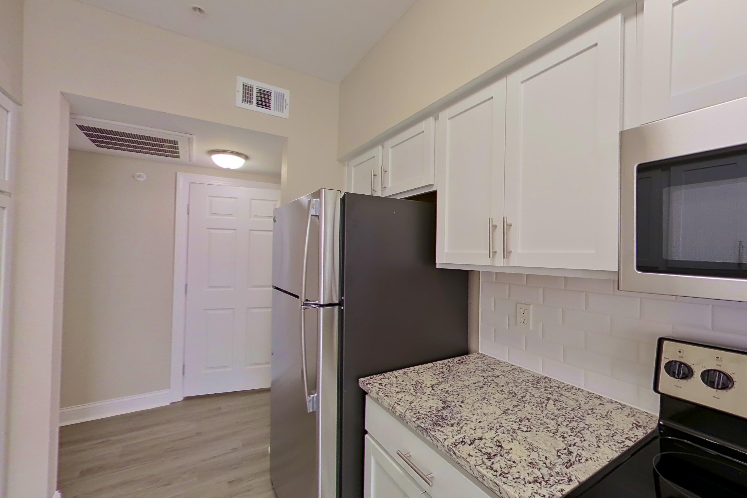 Kitchen with dishwasher, electric range, light stone countertops, light wood-finish flooring, oven/range, refrigerator, and stainless steel appliances, Apartment 6332 at Marq Perimeter
