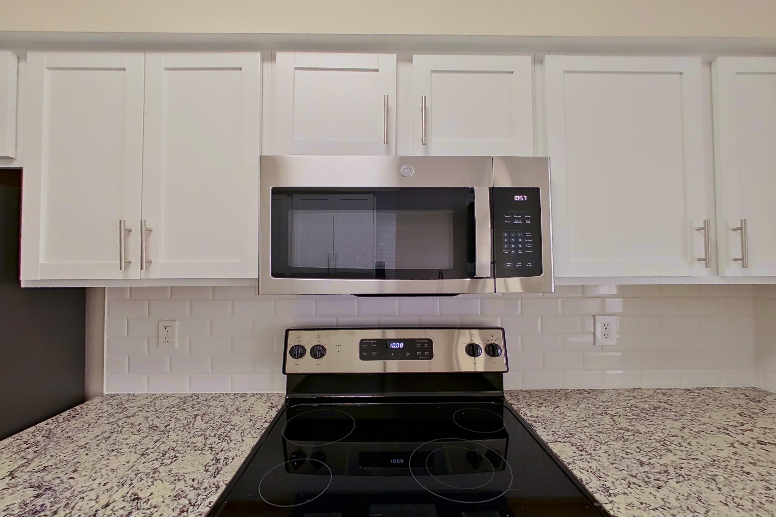Kitchen with dishwasher, electric range, light stone countertops, light wood-finish flooring, oven/range, refrigerator, and stainless steel appliances, Apartment 6332 at Marq Perimeter