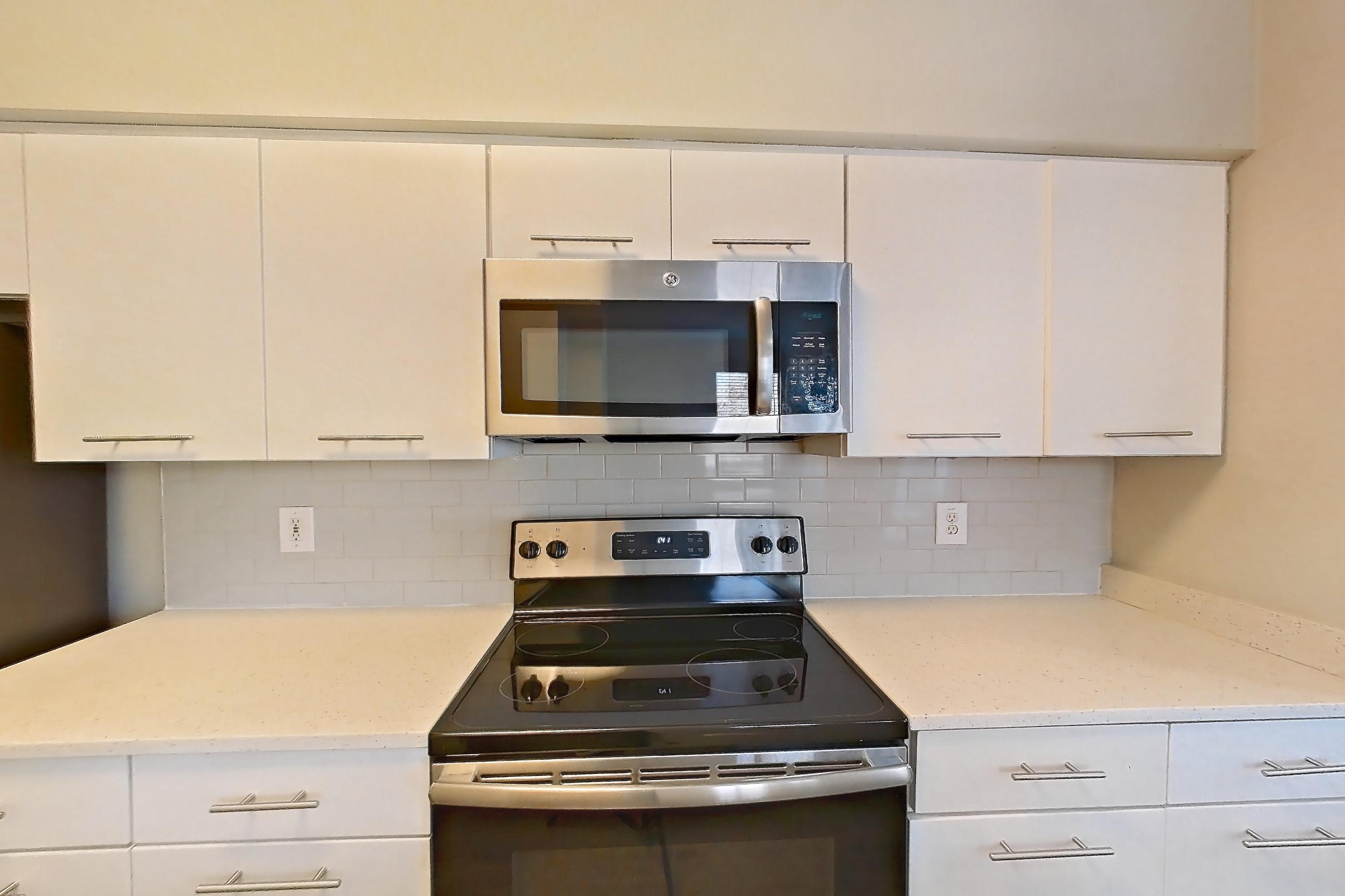 Kitchen with dark wood-finish flooring, electric range, light countertops, light stone countertops, light wood-finish flooring, microwave, oven/range, refrigerator, and stainless steel appliances, Apartment 6336 at Marq Perimeter