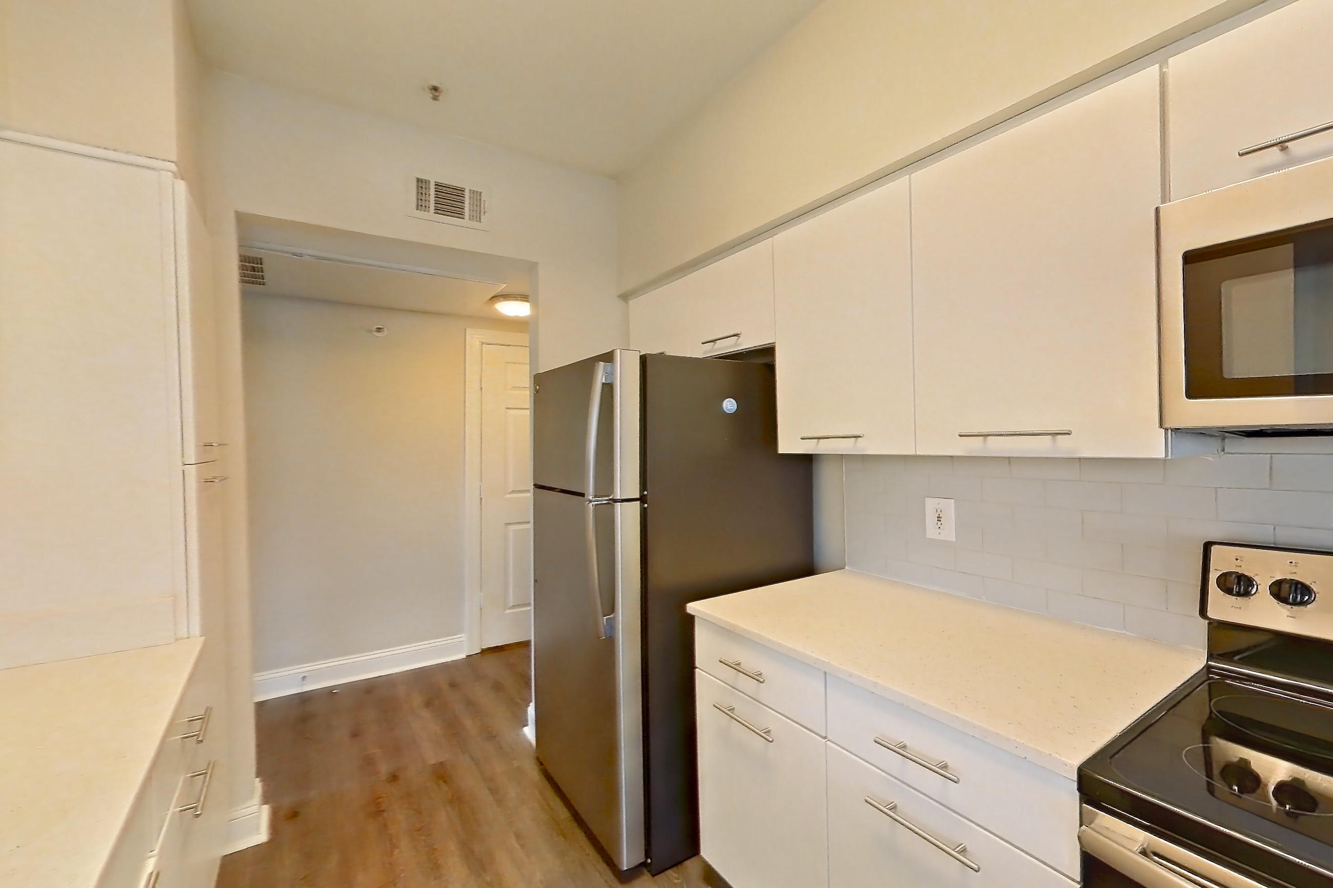 Kitchen with dark wood-finish flooring, electric range, light countertops, light stone countertops, light wood-finish flooring, microwave, oven/range, refrigerator, and stainless steel appliances, Apartment 6336 at Marq Perimeter