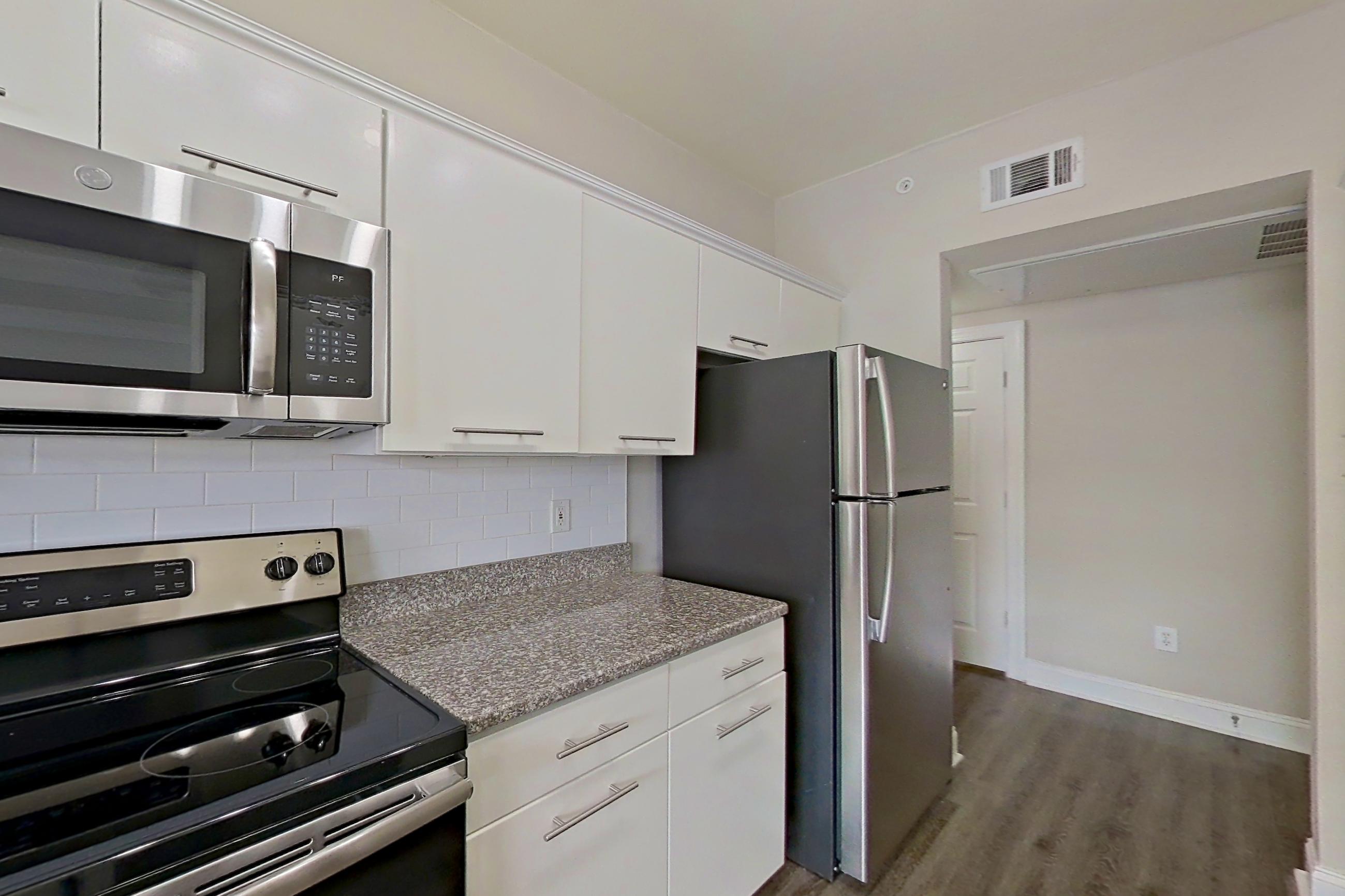 Kitchen with dark stone countertops, electric range, light stone countertops, microwave, oven/range, refrigerator, and stainless steel appliances, Apartment 6419 at Marq Perimeter