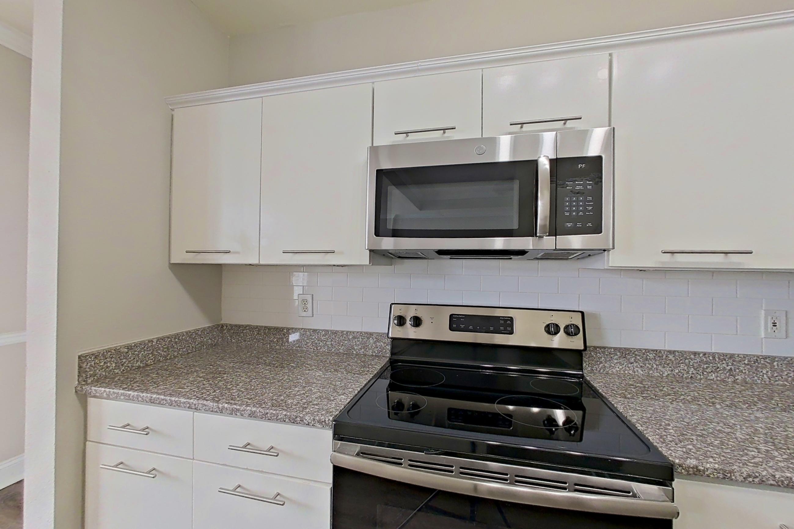Kitchen with dark stone countertops, electric range, light stone countertops, microwave, oven/range, refrigerator, and stainless steel appliances, Apartment 6419 at Marq Perimeter