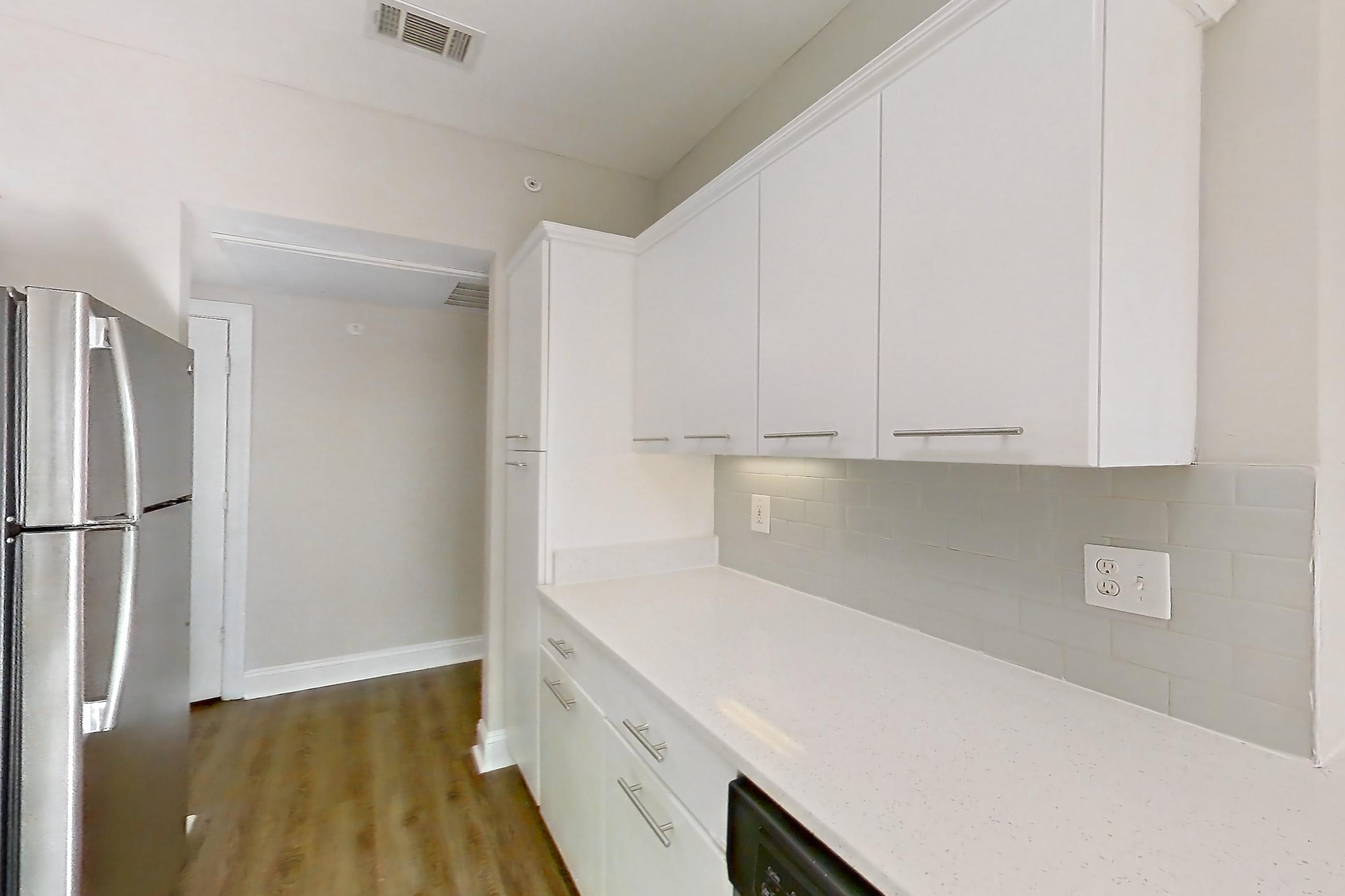 Kitchen with black appliances, dishwasher, electric range, light countertops, light stone countertops, light wood-finish flooring, microwave, oven/range, refrigerator, and stainless steel appliances, Apartment 6425 at Marq Perimeter