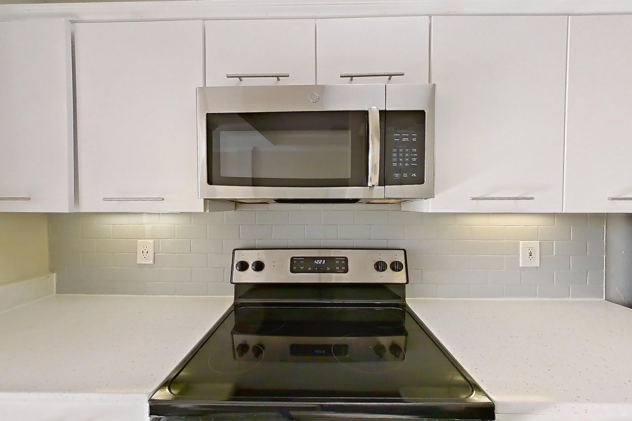 Kitchen with black appliances, dishwasher, electric range, light countertops, light stone countertops, light wood-finish flooring, microwave, oven/range, refrigerator, and stainless steel appliances, Apartment 6425 at Marq Perimeter