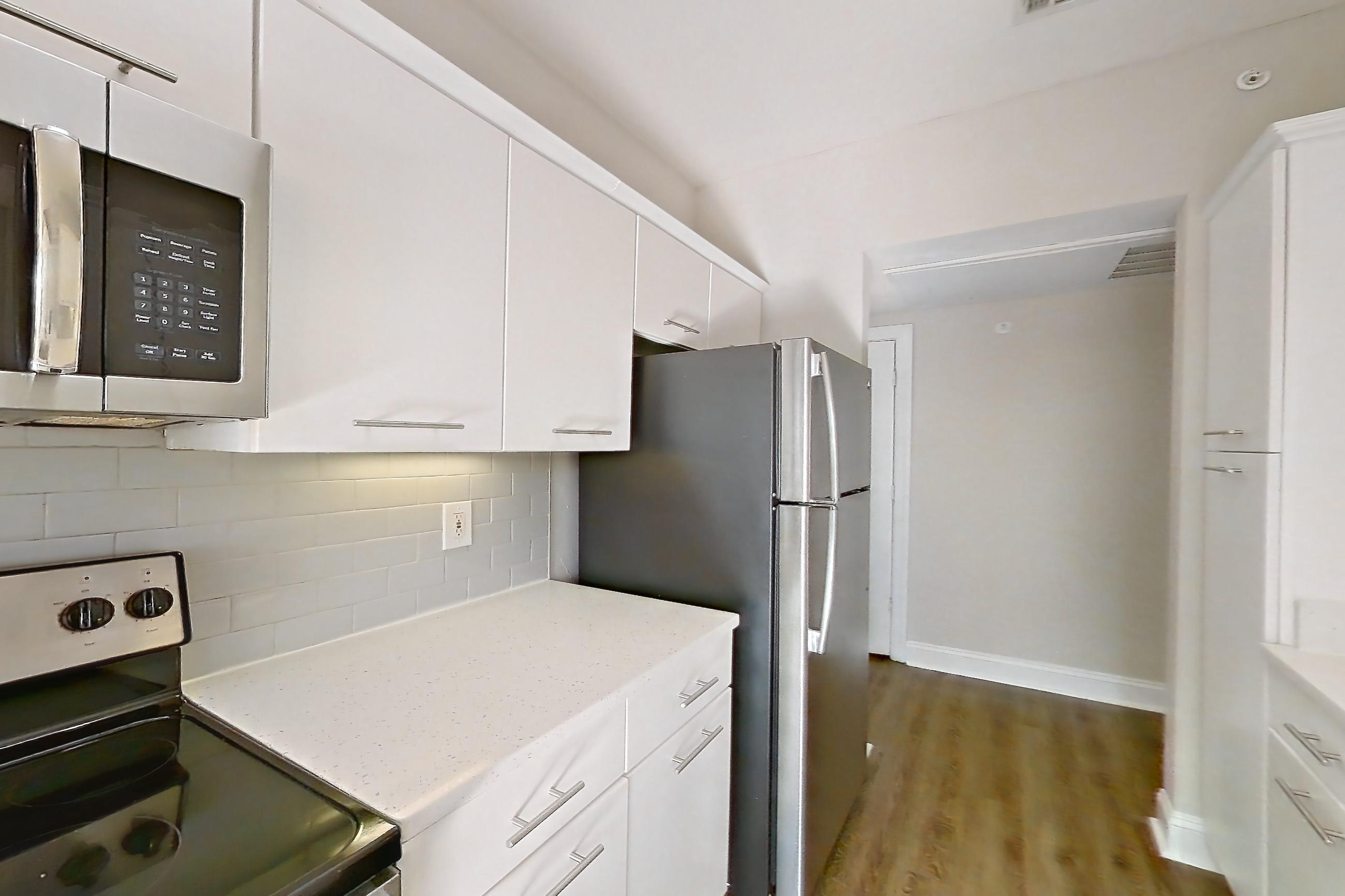 Kitchen with black appliances, dishwasher, electric range, light countertops, light stone countertops, light wood-finish flooring, microwave, oven/range, refrigerator, and stainless steel appliances, Apartment 6425 at Marq Perimeter
