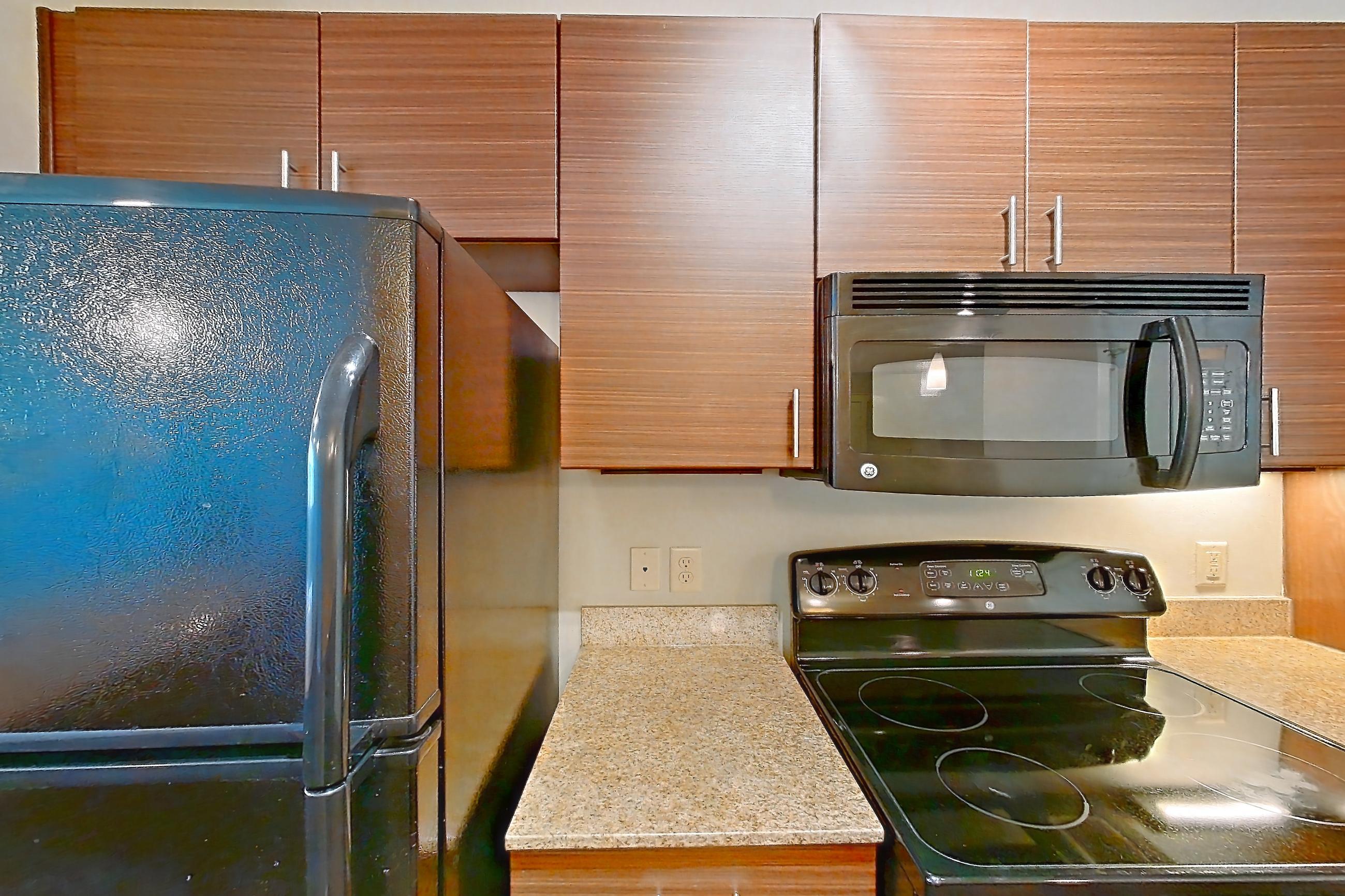Kitchen with black appliances, dark wood-finish flooring, dishwasher, electric range, light countertops, light stone countertops, microwave, oven/range, and refrigerator, Apartment 04306 at Marquis Cresta Bella